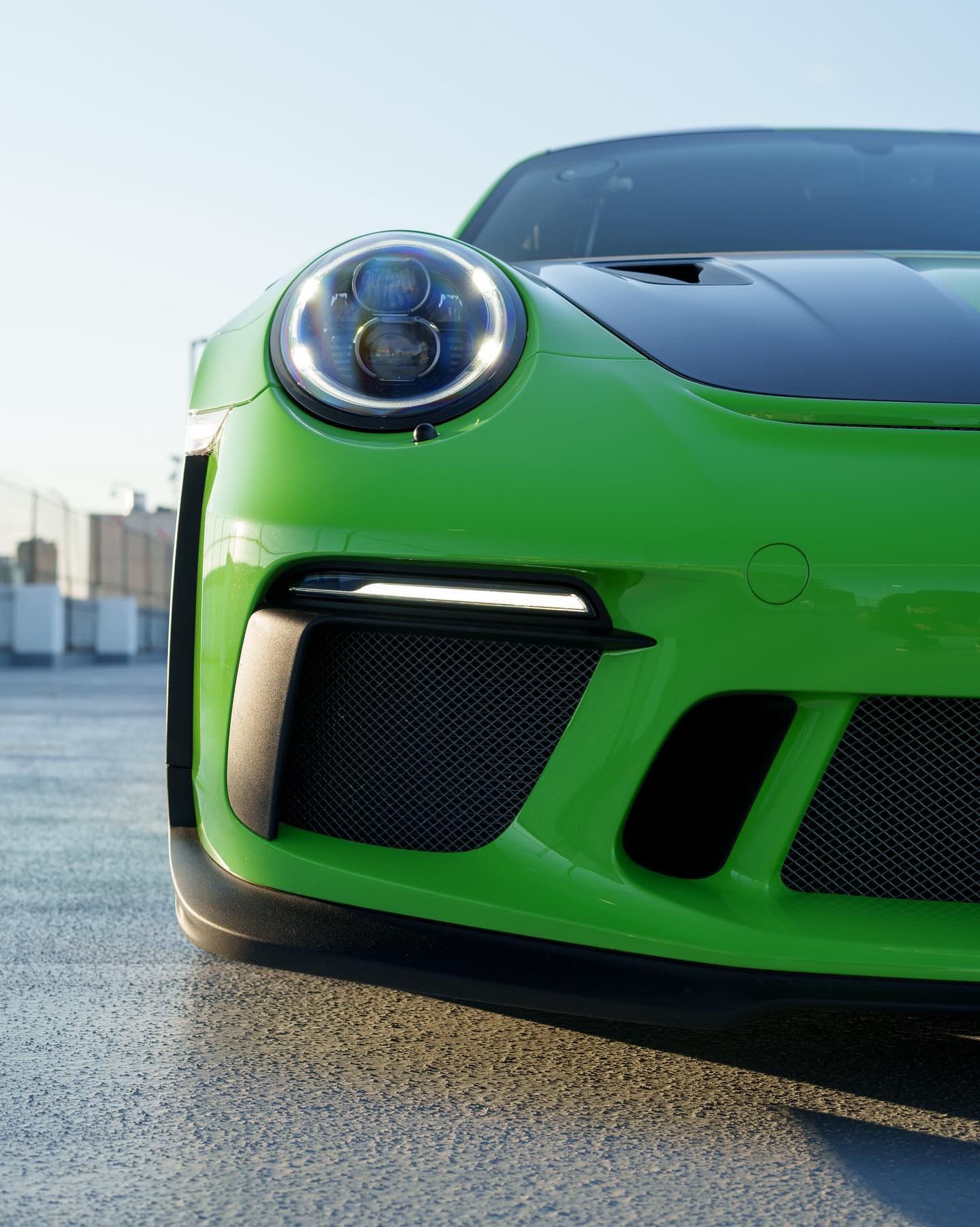 Close-up of a bright green sports car’s front end on a wet road, with one headlight and grille visible