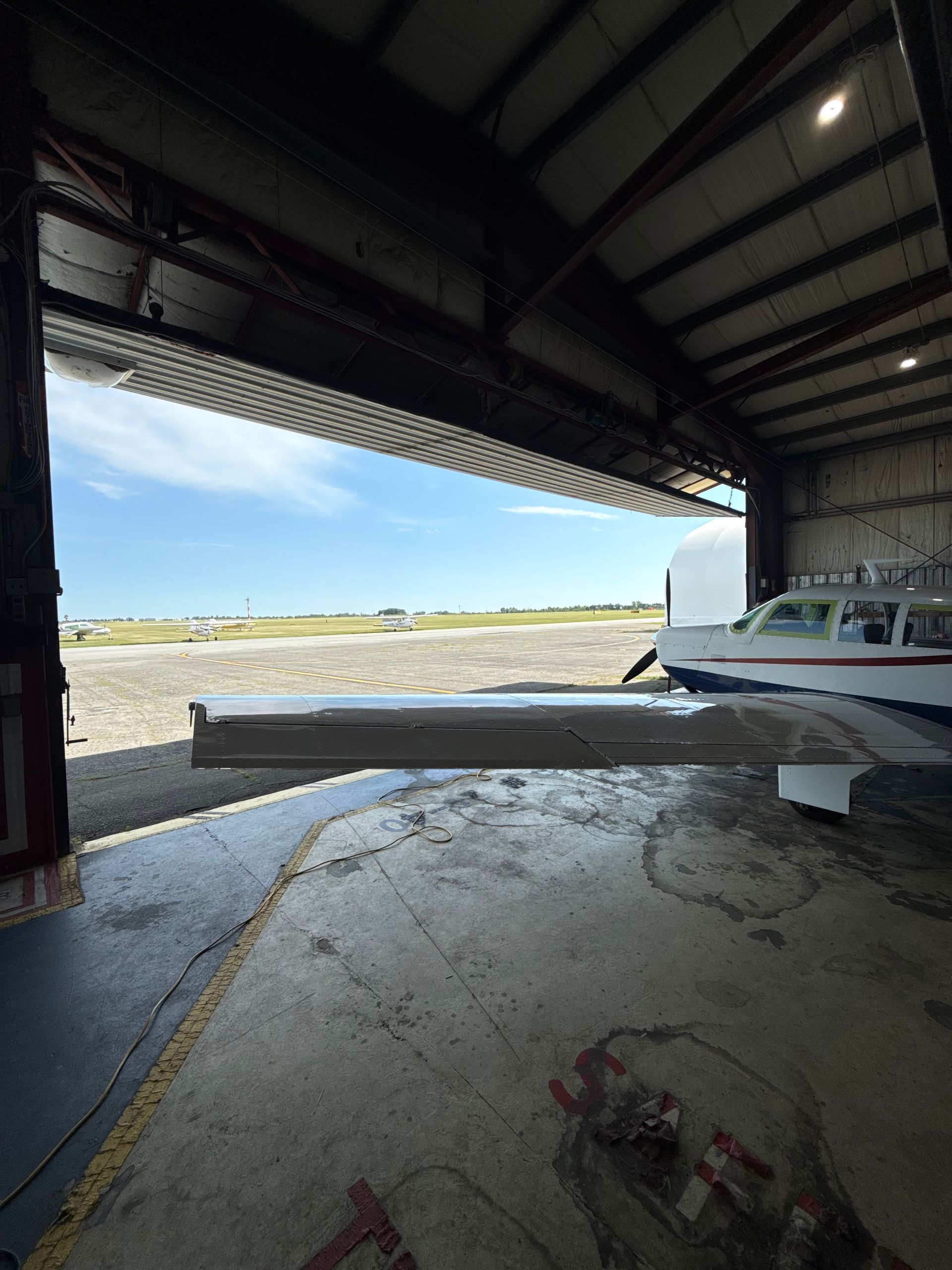 Inside a hangar, a small white airplane sits on the right with bright airfield visible outside.
