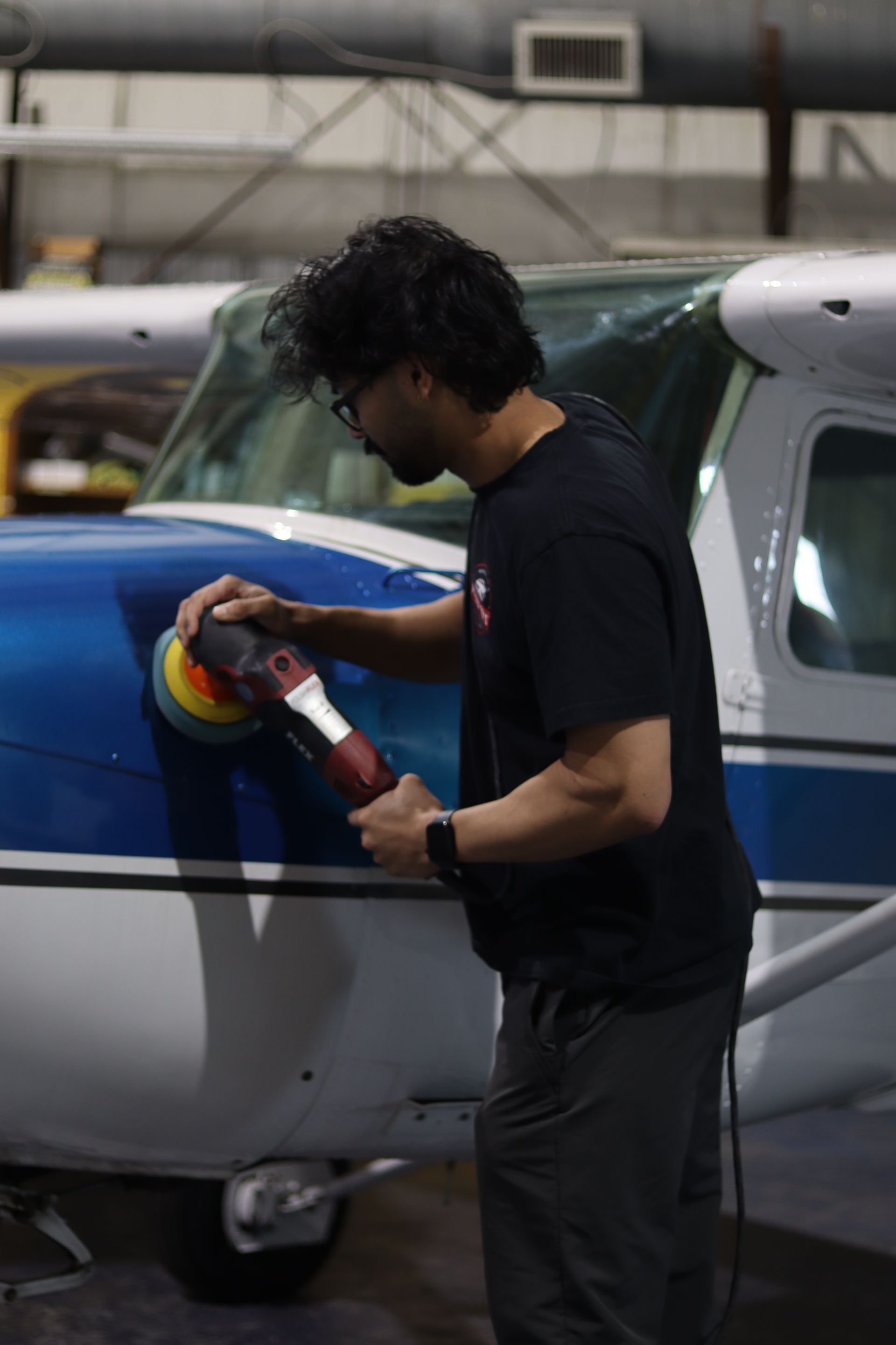 Person polishing the blue fuselage of a small airplane in a hangar
