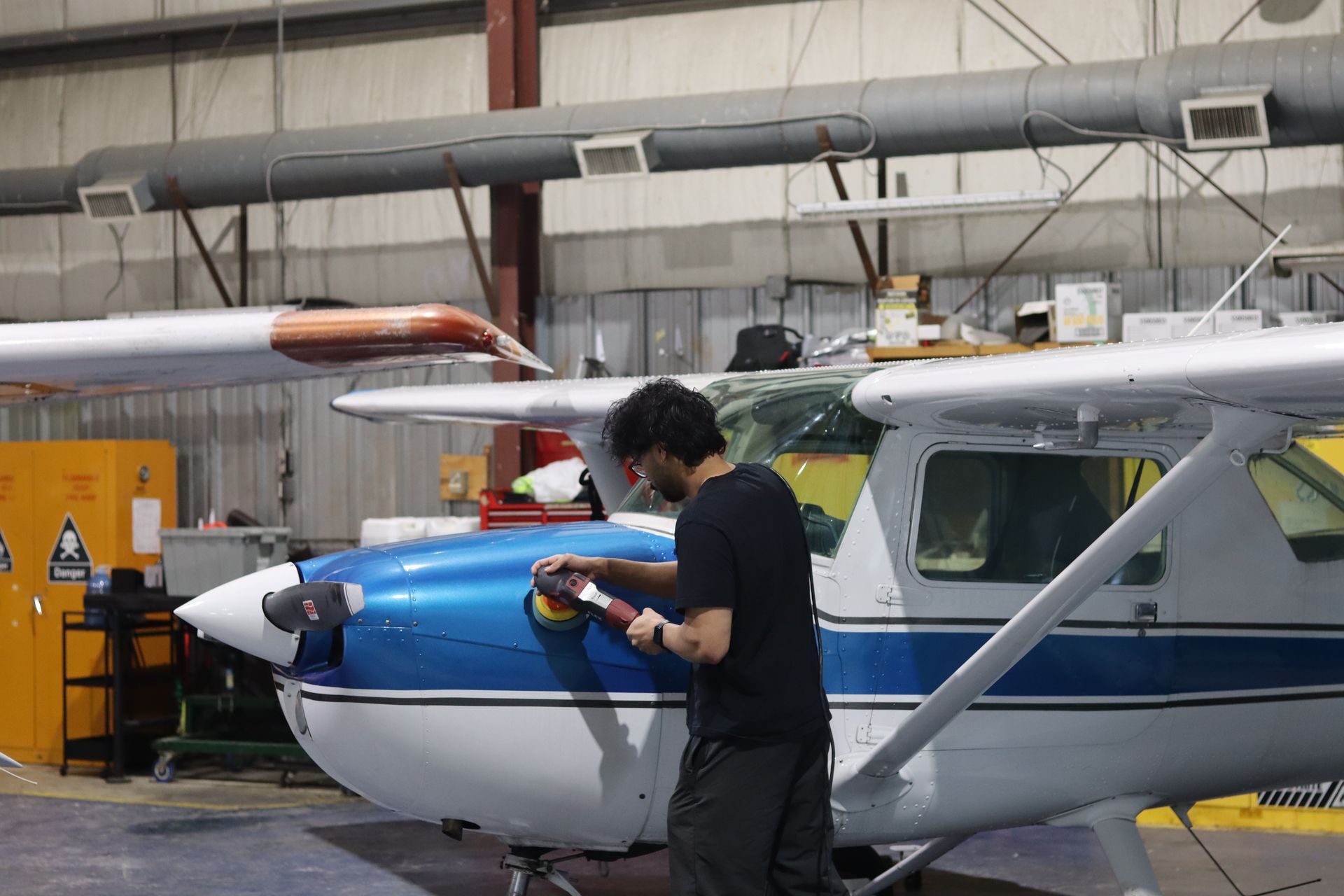 Person working on the nose of a blue-and-white small airplane inside a hangar