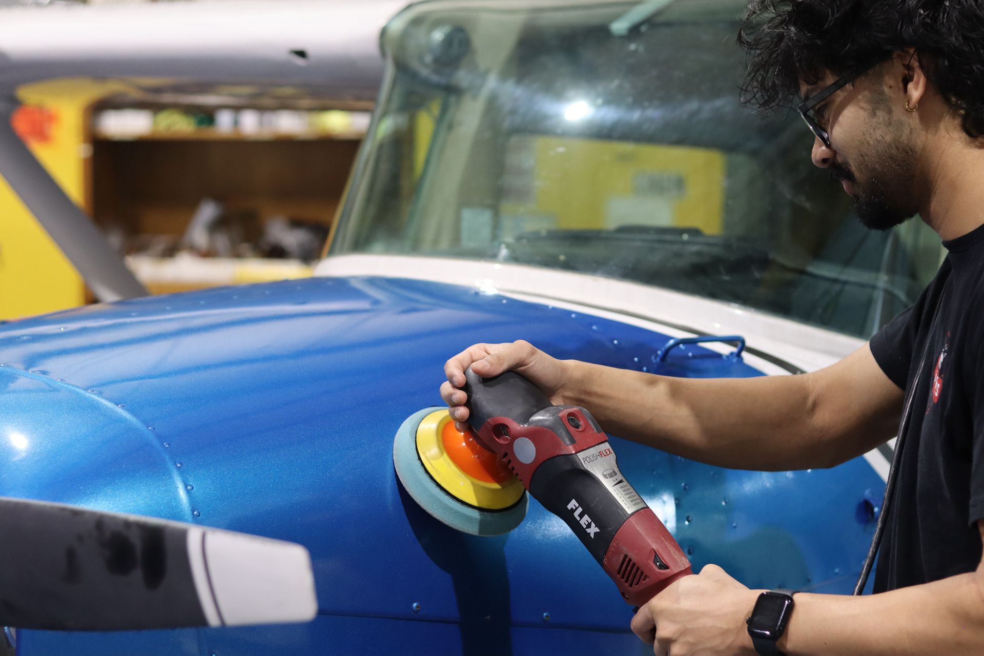 Person using a power buffer to polish a blue car hood in a workshop