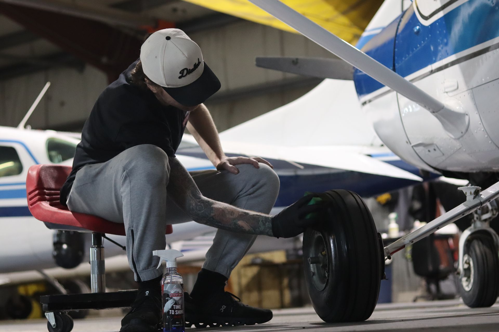 Technician inspecting a small airplane wheel beside a blue-and-white aircraft in a hangar