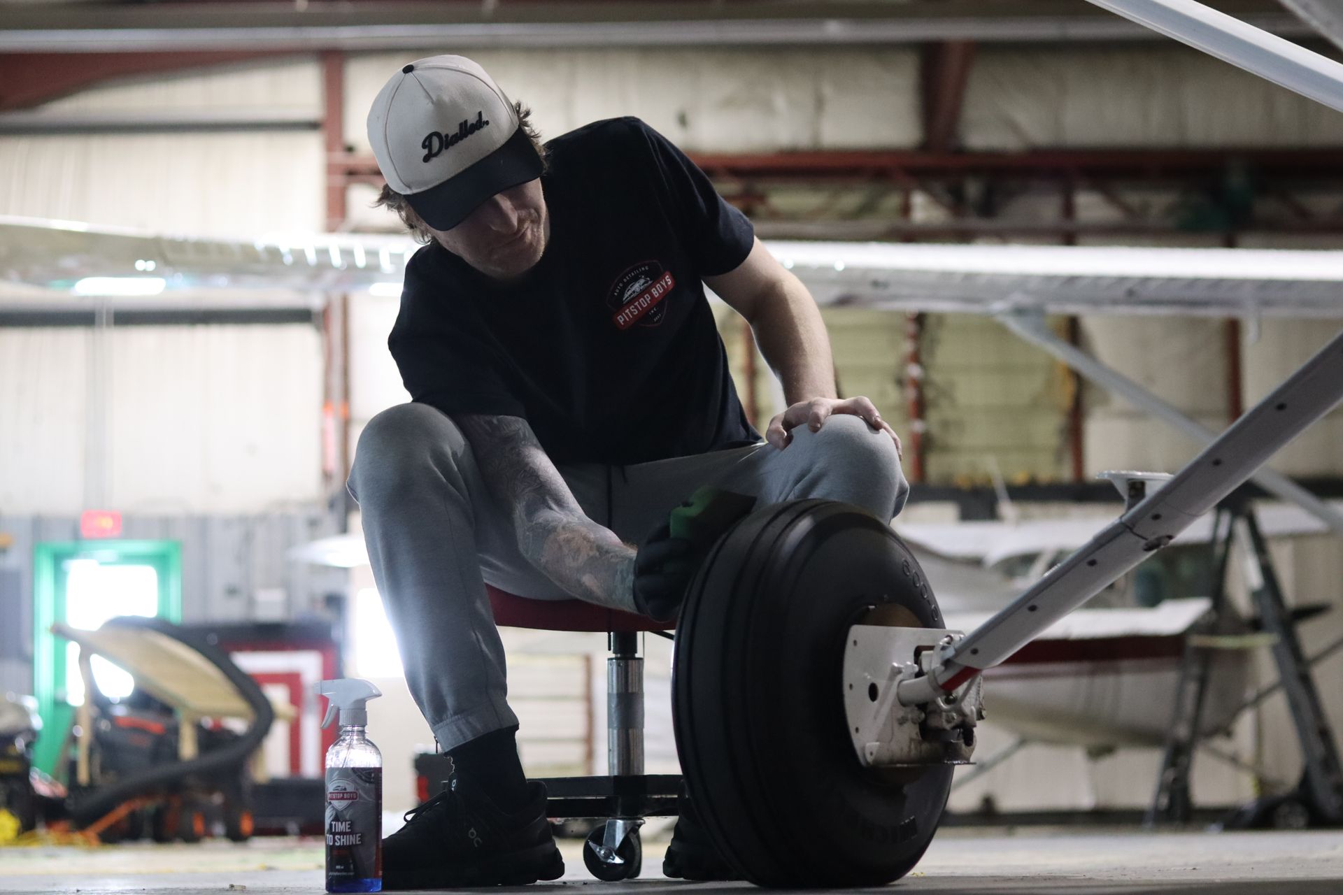 Mechanic tightening a tire on a race car in a workshop, wearing a cap and dark shirt