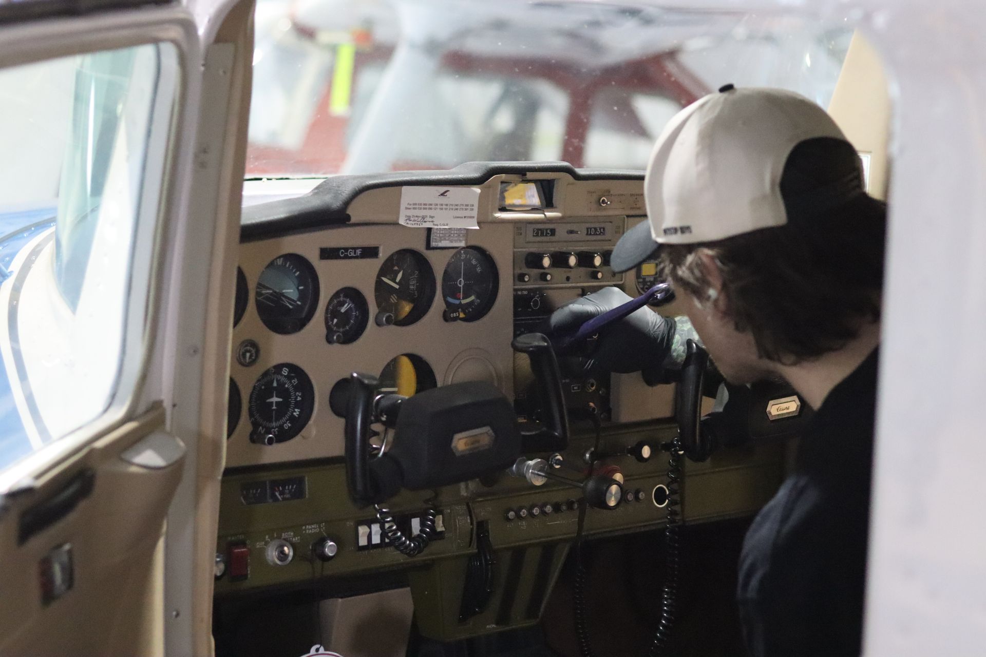 Person in a white cap sitting in a small airplane cockpit, looking at the instrument panel.