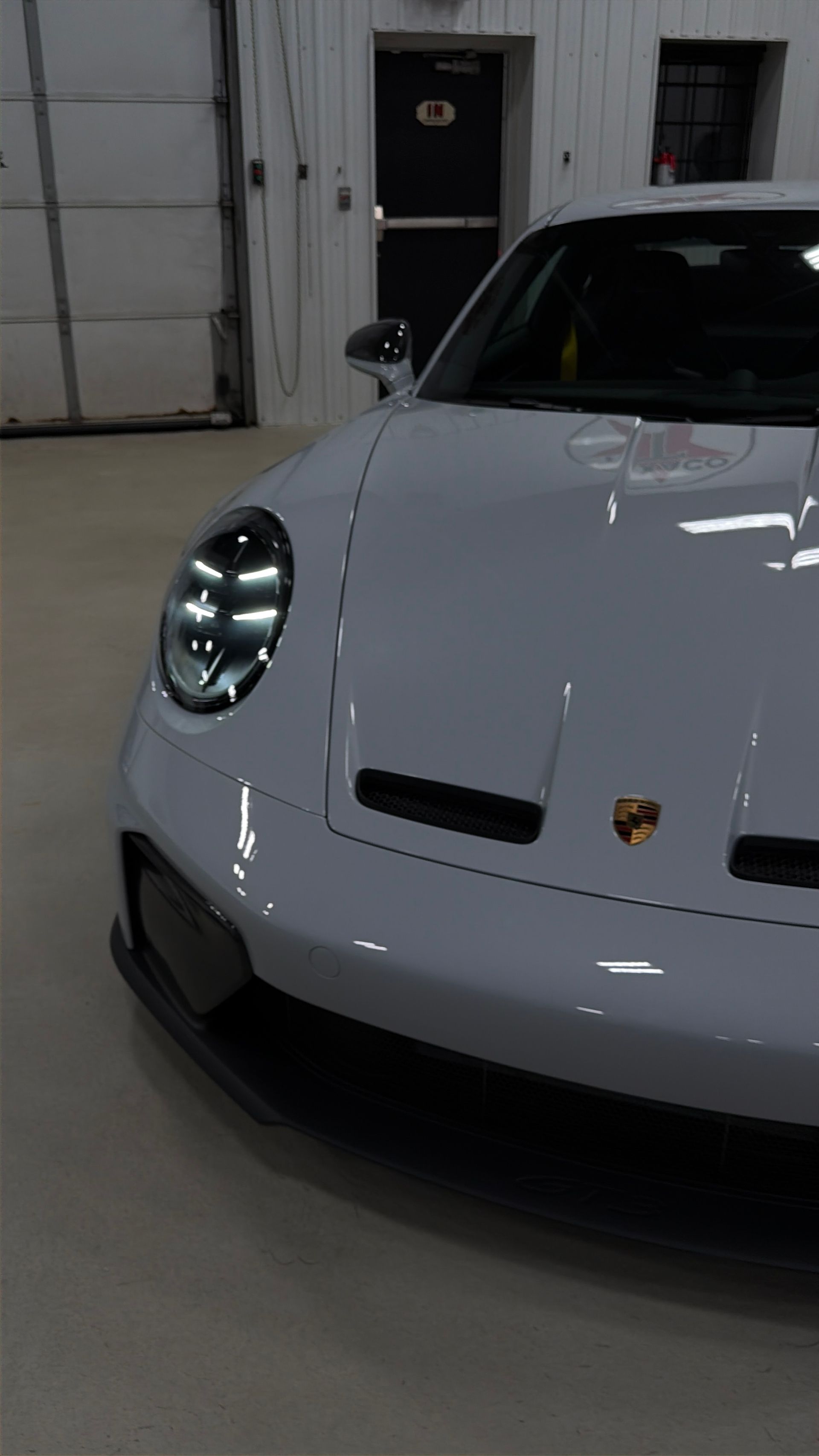 Front view of a white Porsche sports car parked indoors near a garage door.