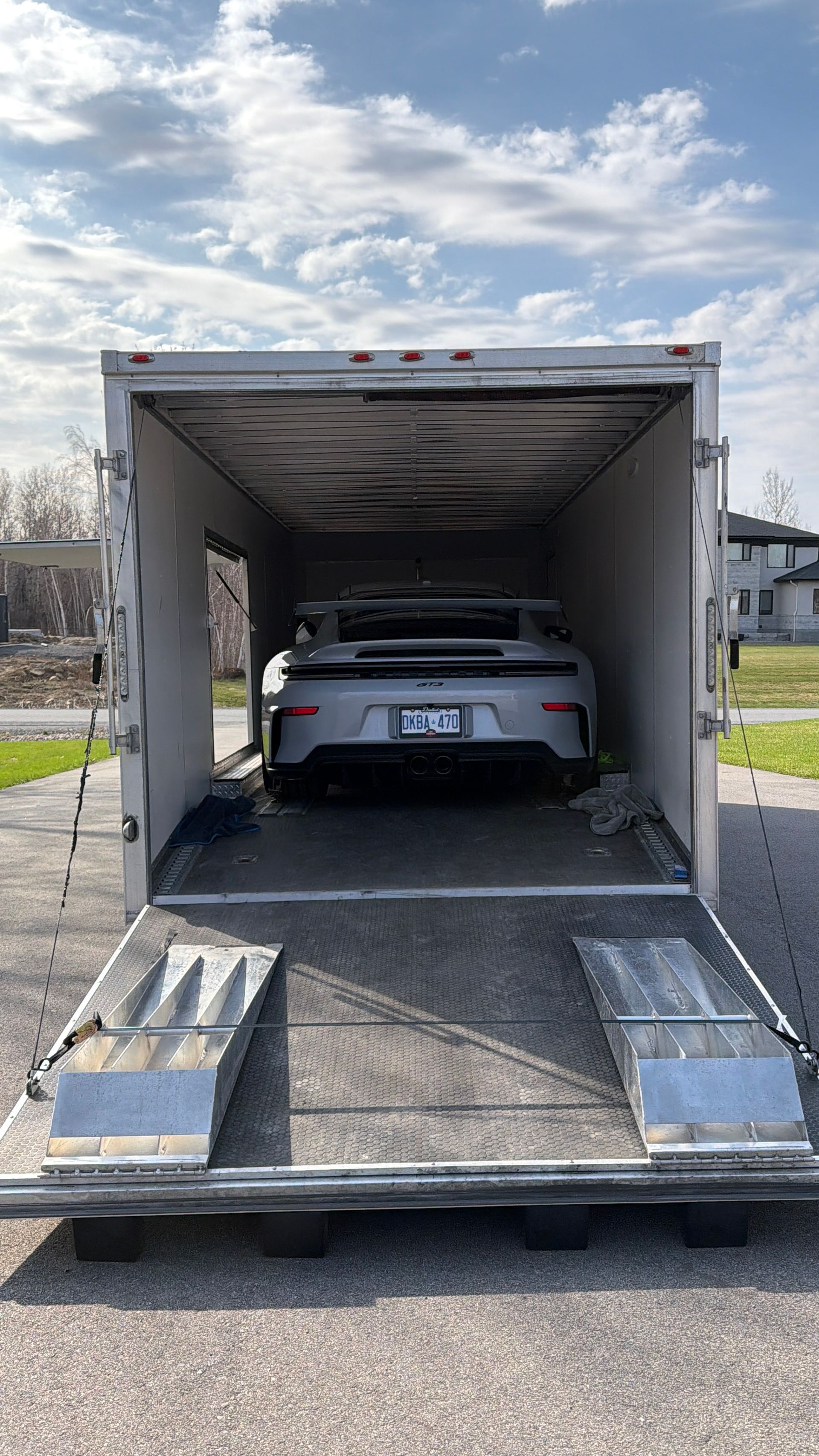 White car inside an enclosed trailer, viewed from the open rear ramp outdoors.