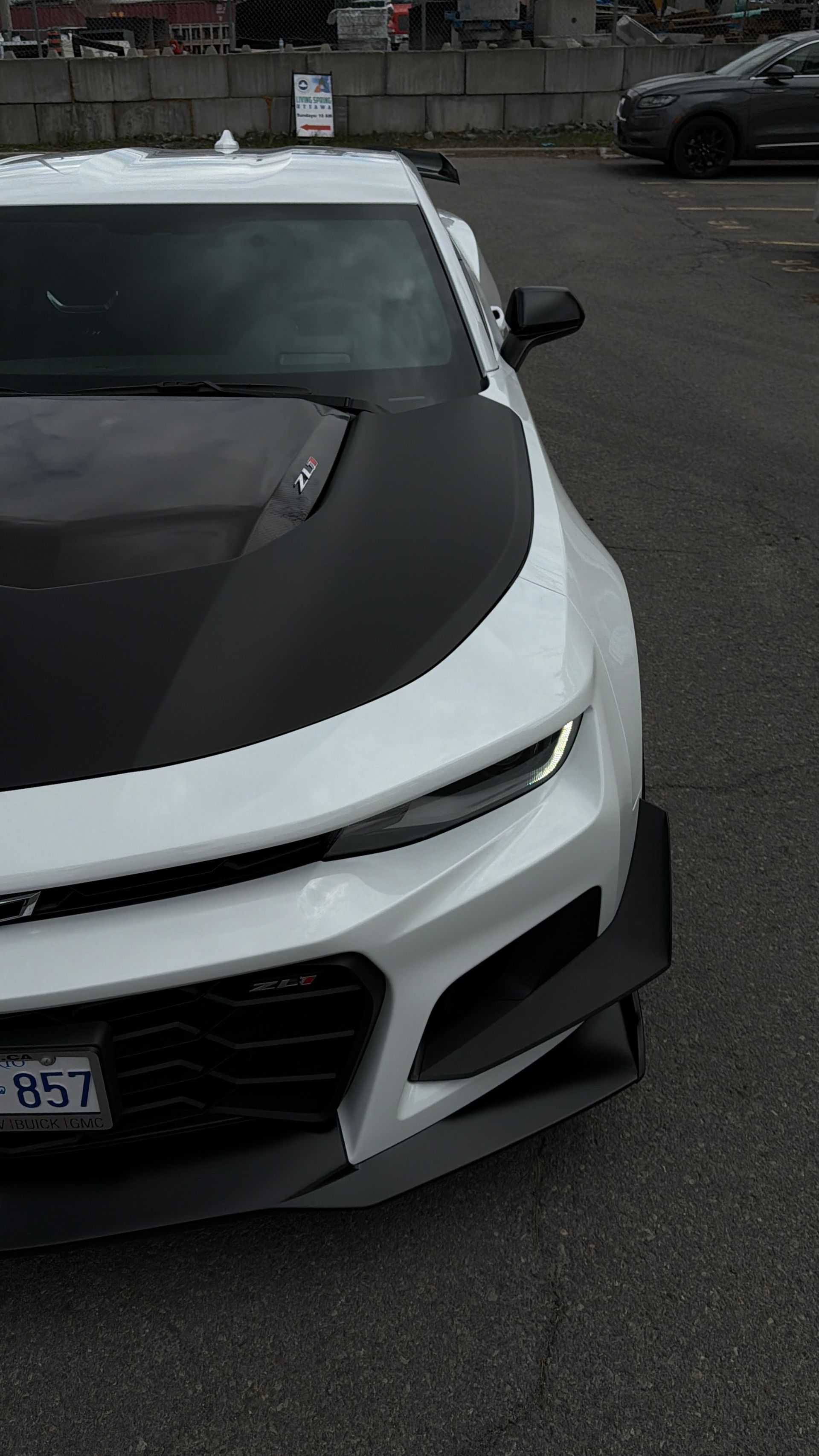 White sports car with black hood parked on wet pavement in a lot