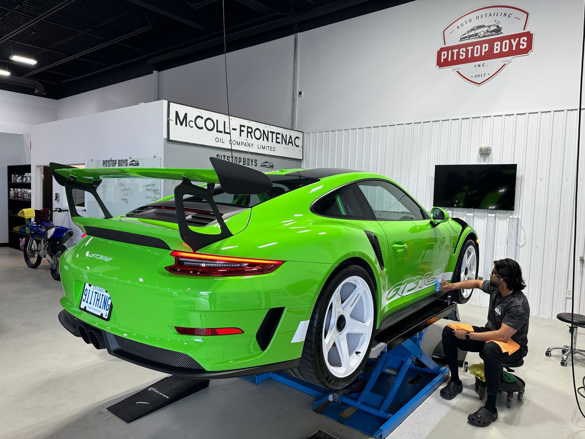 Bright green sports car on a lift in an auto shop, with a mechanic working by the rear wheel.