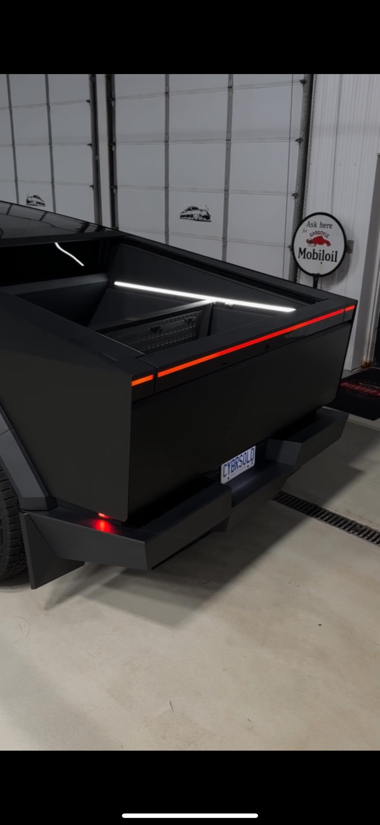 Black futuristic sports car parked in a garage, rear view with red taillights and glowing trim