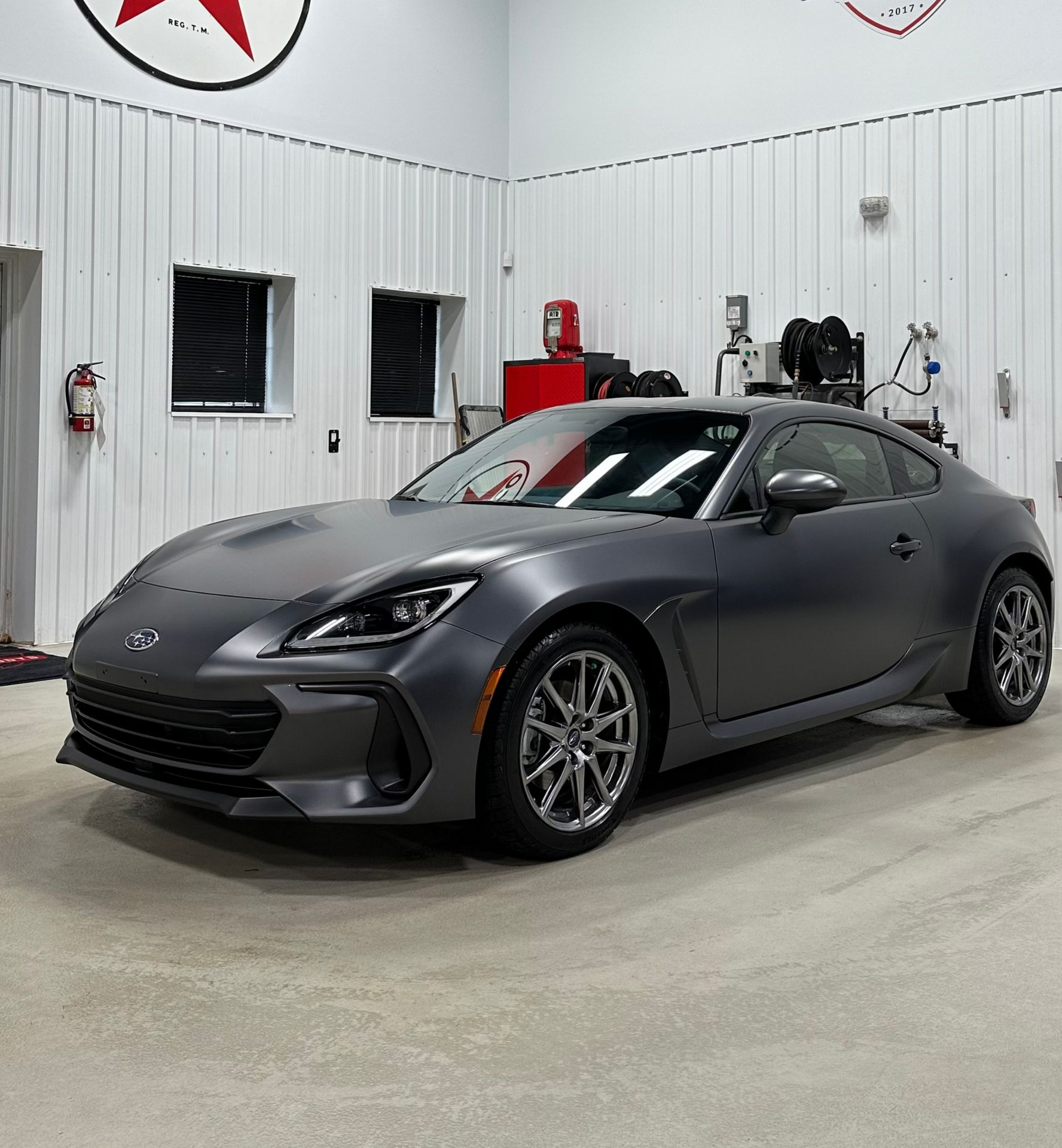 Dark gray sports coupe parked in a white garage, front-left view