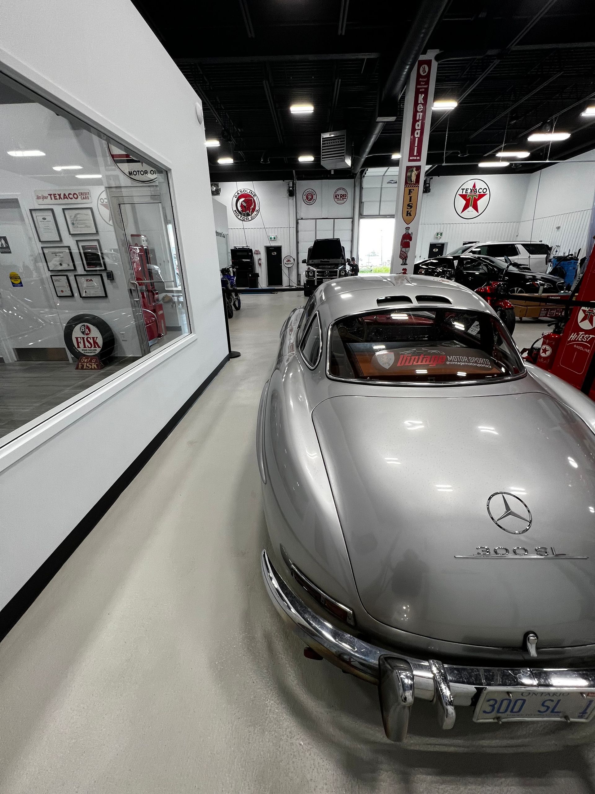 Silver vintage Mercedes-Benz in a showroom, viewed from the rear beside a wall display.