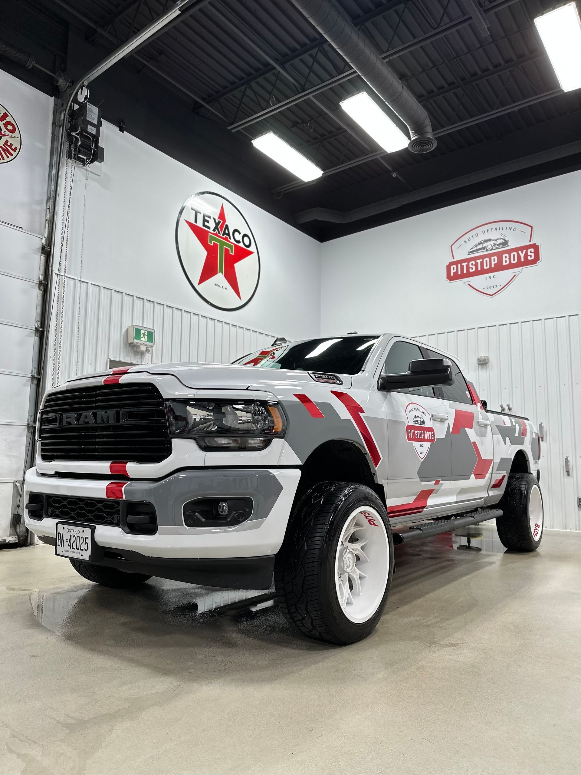 White Chevrolet pickup with red and gray camo decals in a garage showroom, front three-quarter view