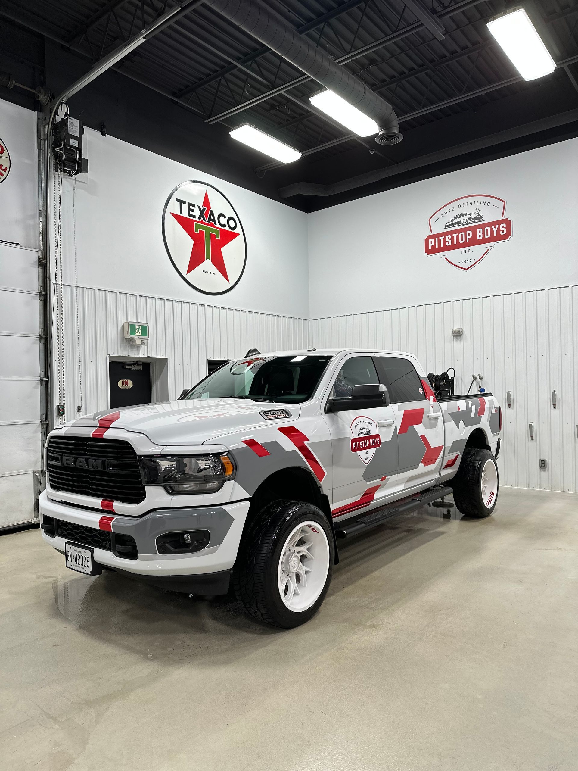 White and red lifted pickup truck in a garage showroom with Team logo wall signs.
