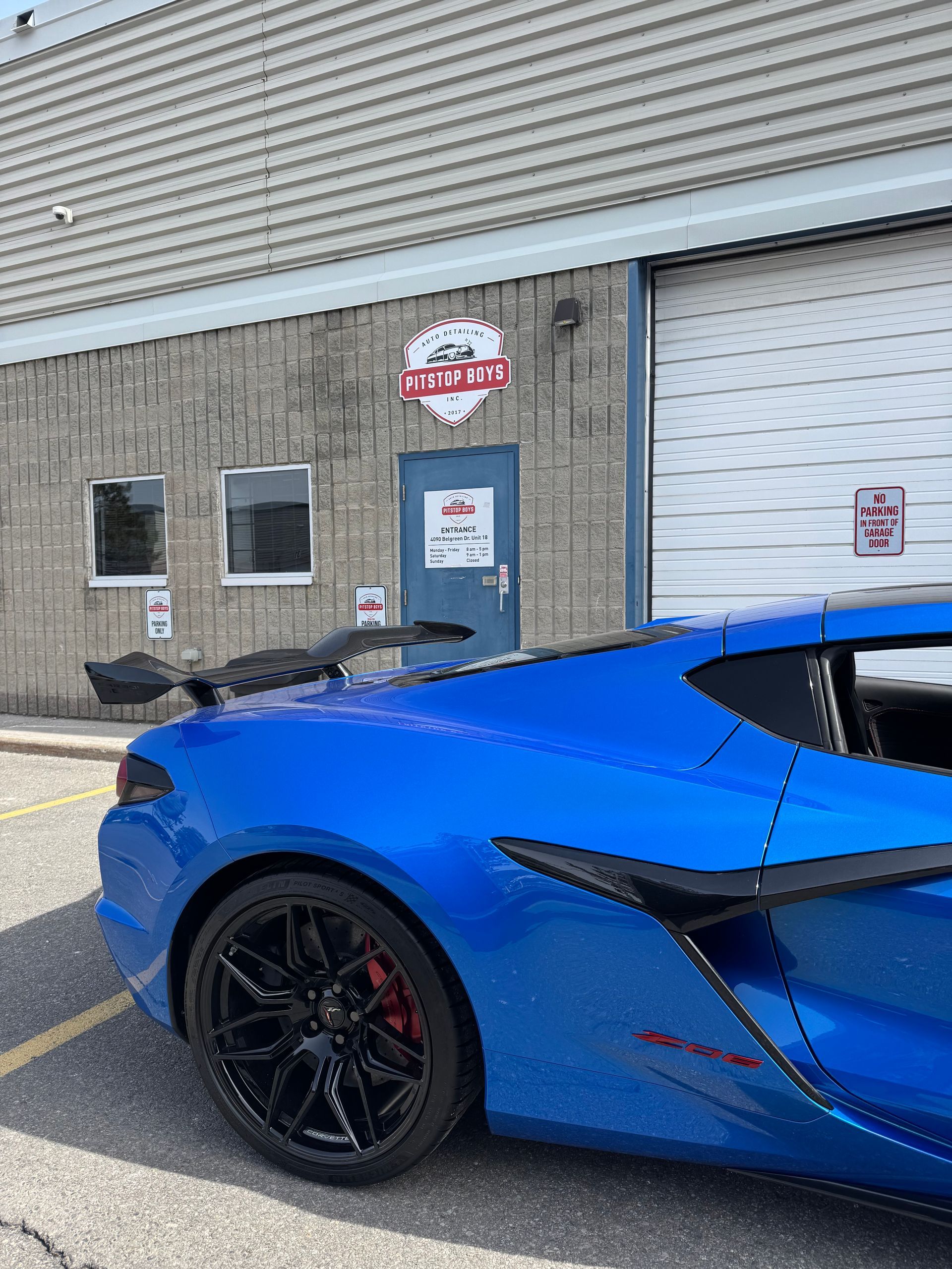 Blue sports car parked outside a warehouse-style building with a gray wall and blue door.
