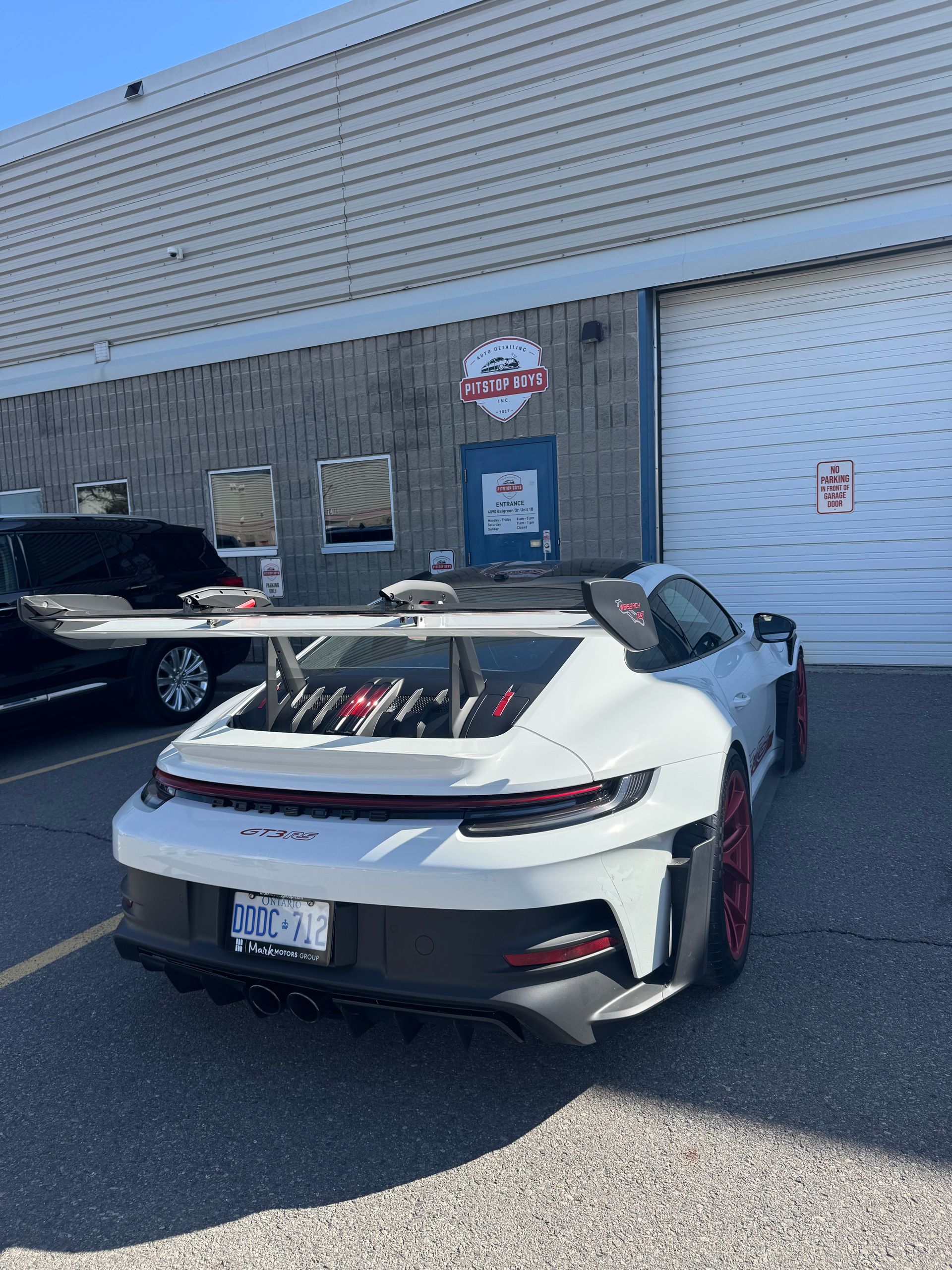 White sports car parked outside a gray building with a blue door and sign.