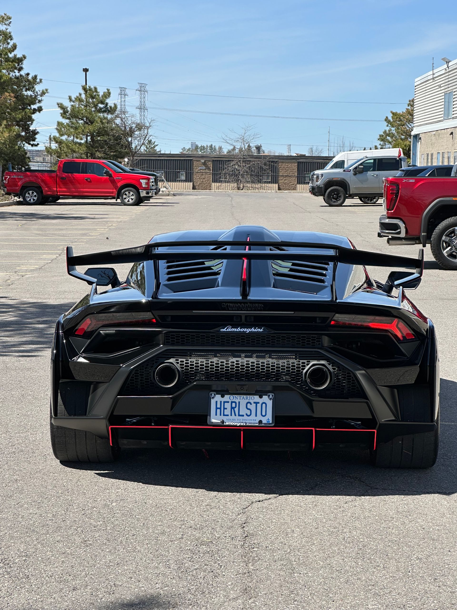 Black sports car rear view in a parking lot with a large spoiler and red accents
