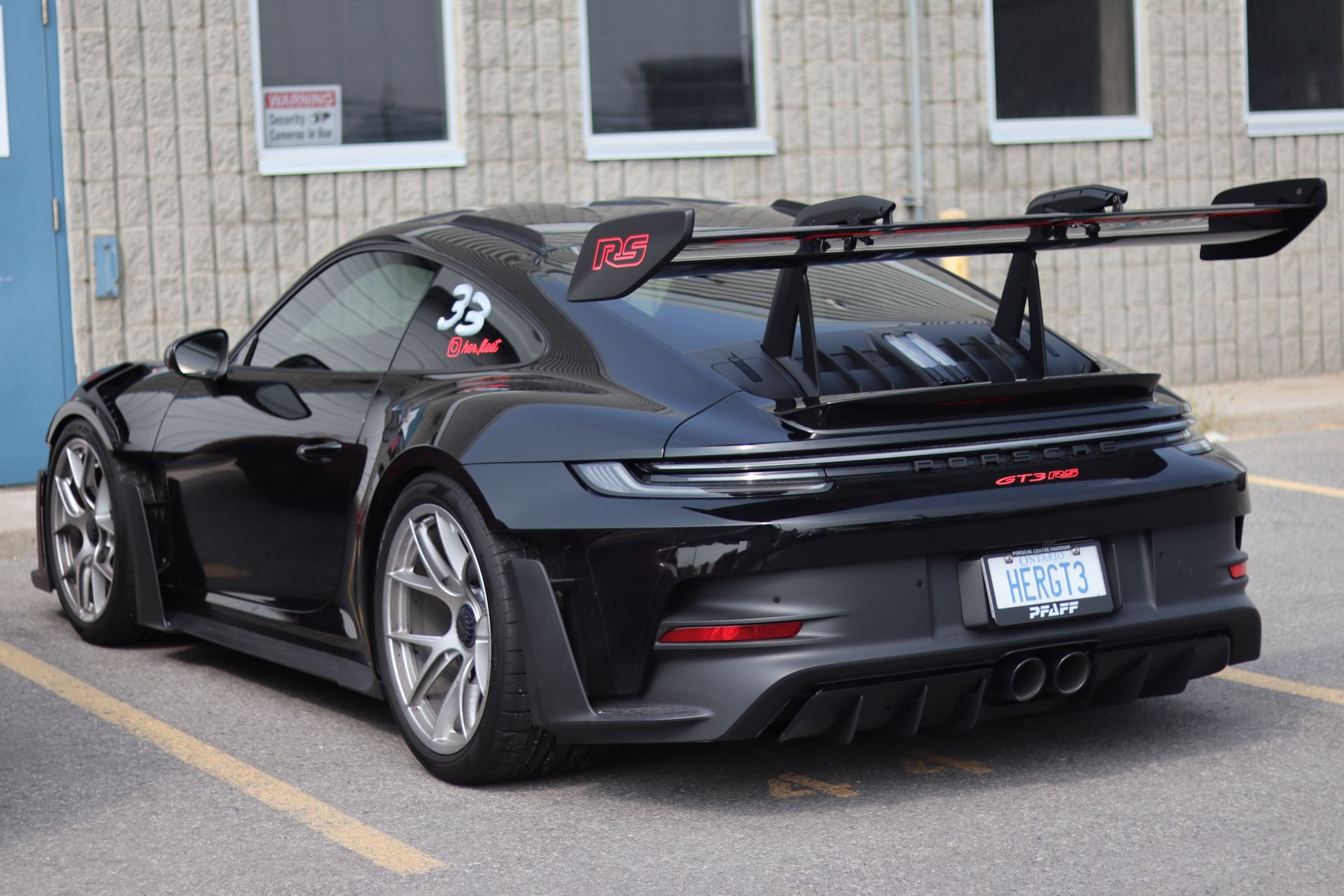 Black sports car with a large rear wing parked beside a building.