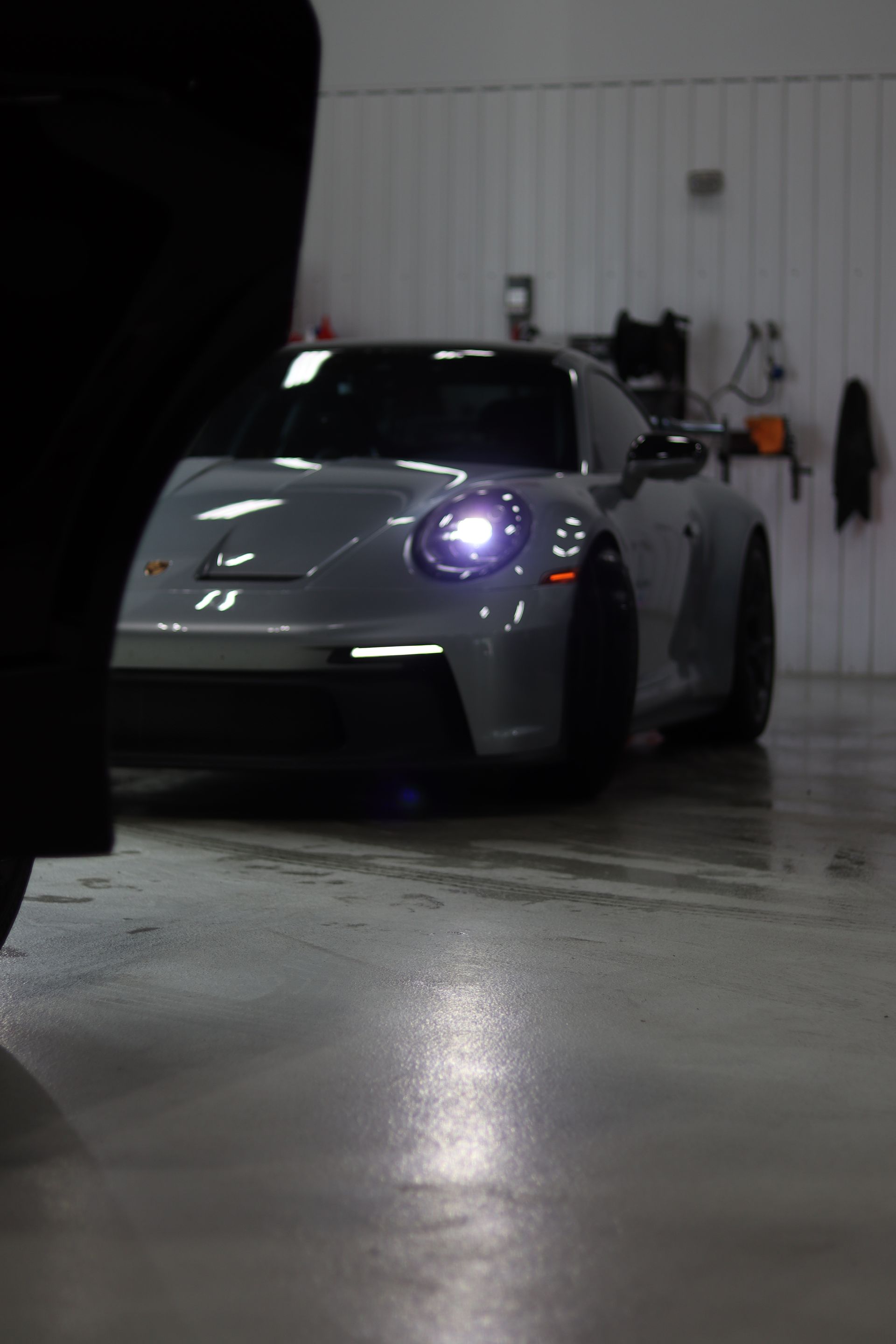 Silver sports car in a garage, facing forward with headlights on.