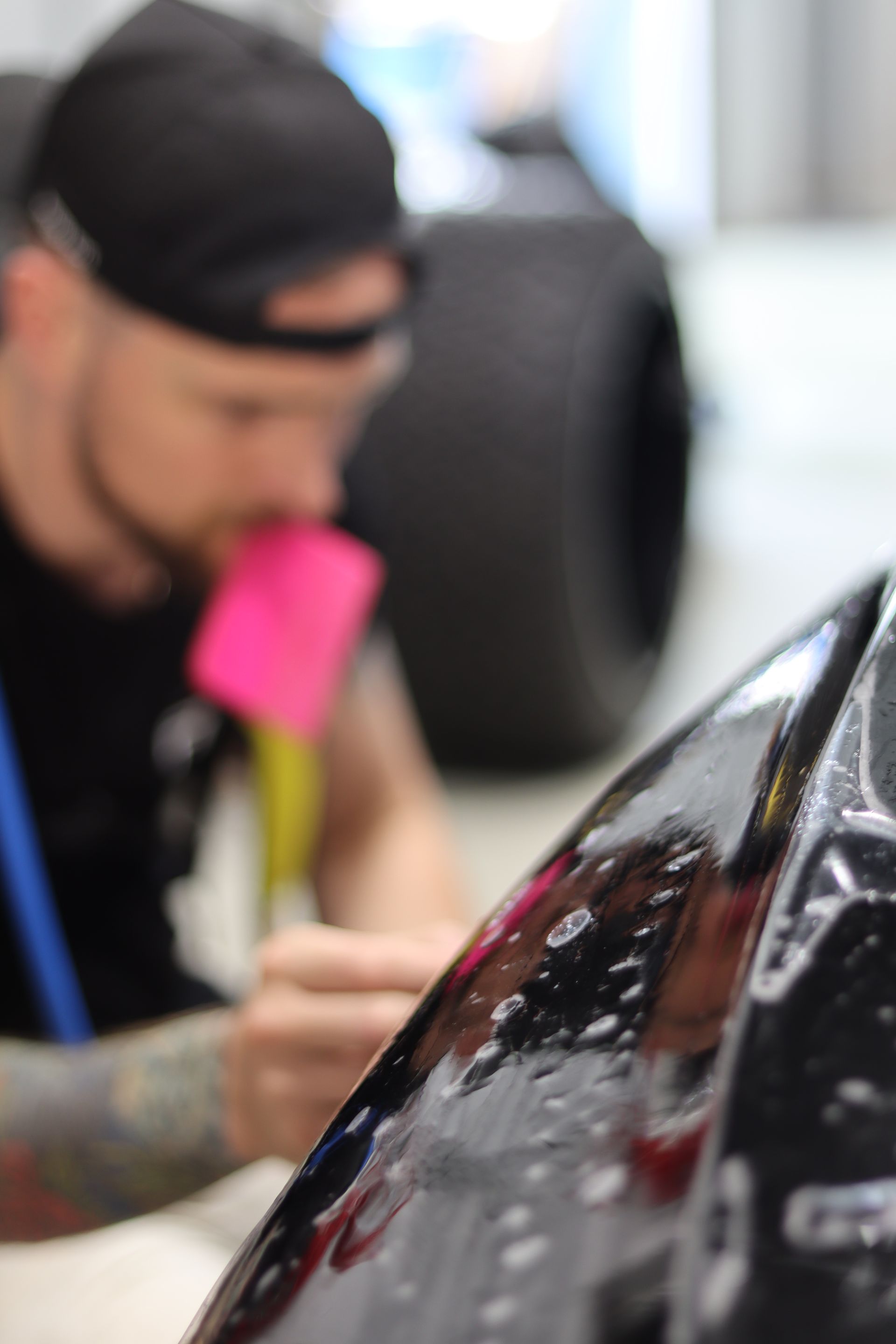 Man polishing a black car hood with a pink cloth in an auto shop