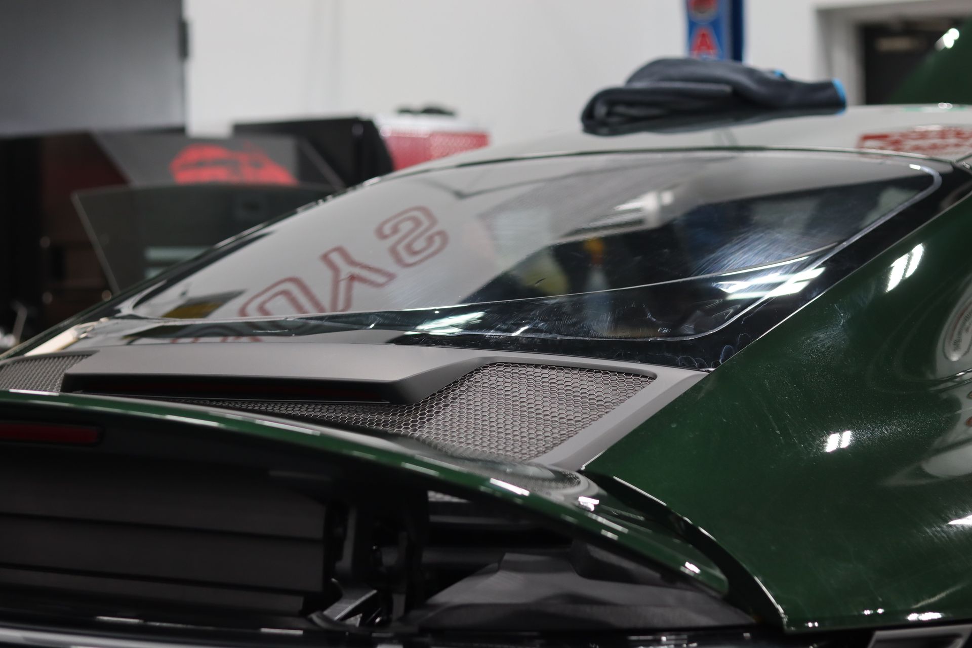 Close-up of a glossy dark green sports car hood and windshield in a garage