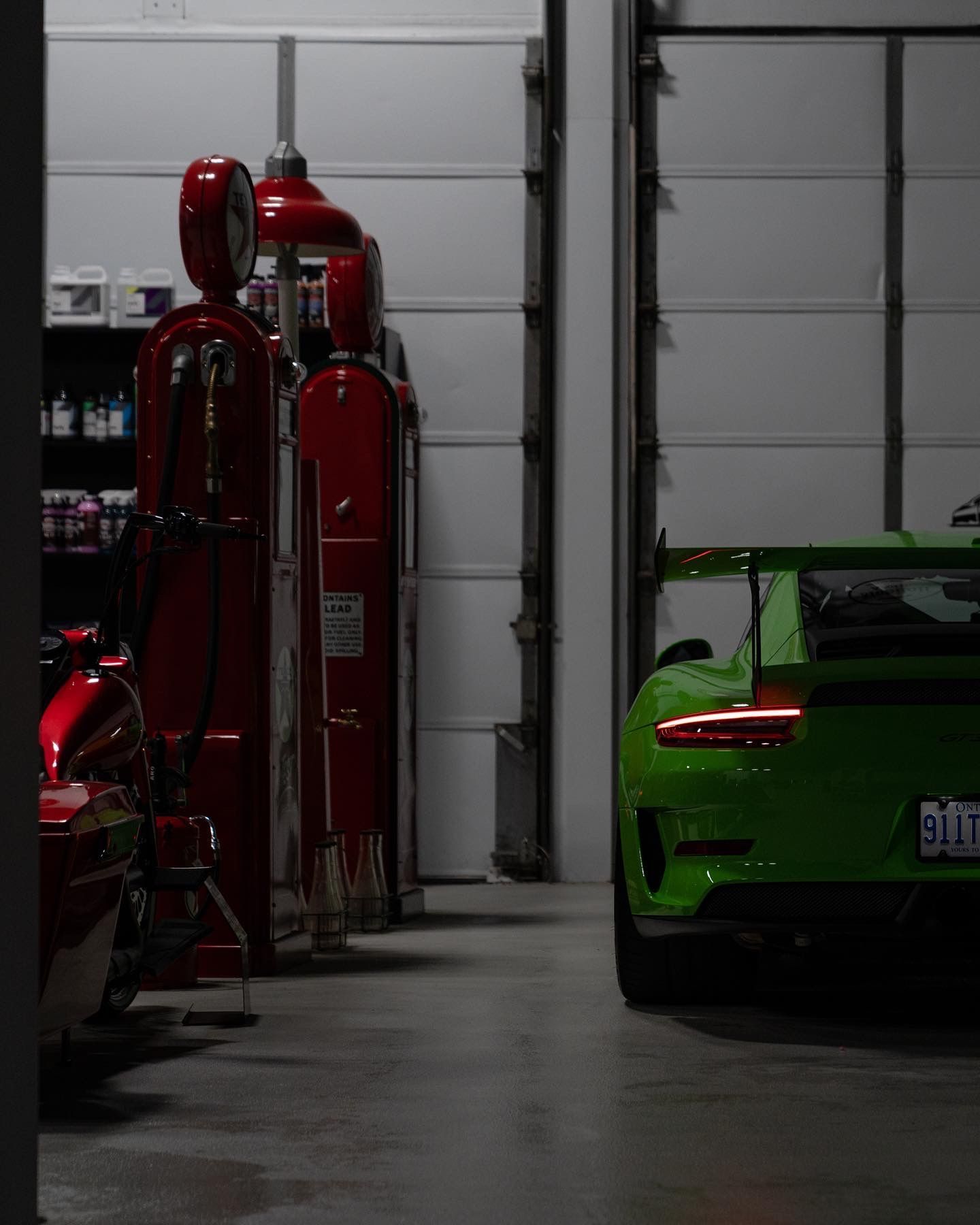 Green sports car beside red gas pumps in a dim garage