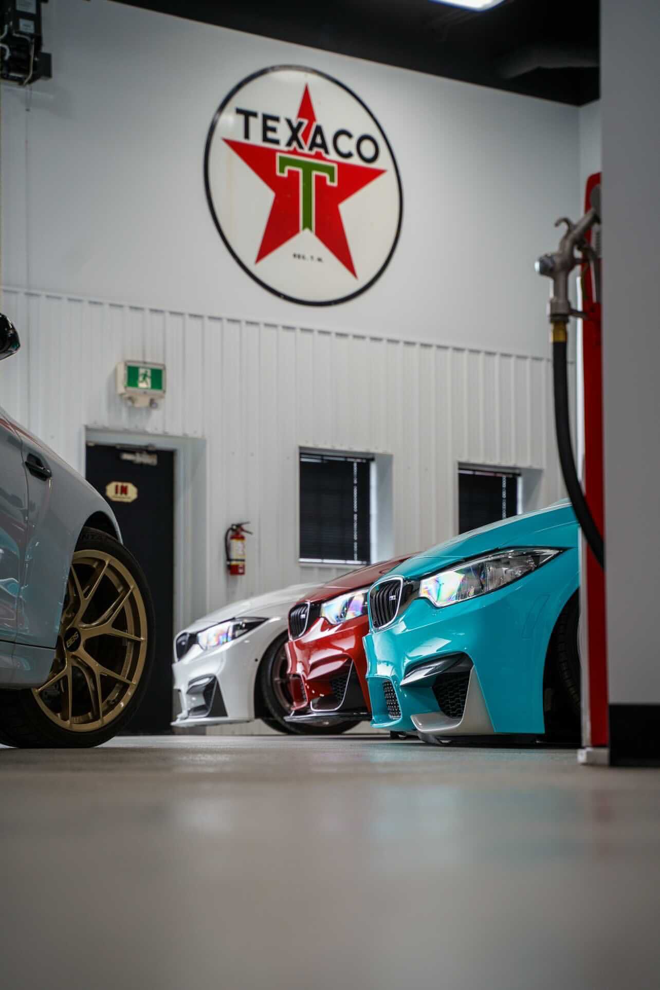 Three sports cars in a garage beneath a large Texaco sign