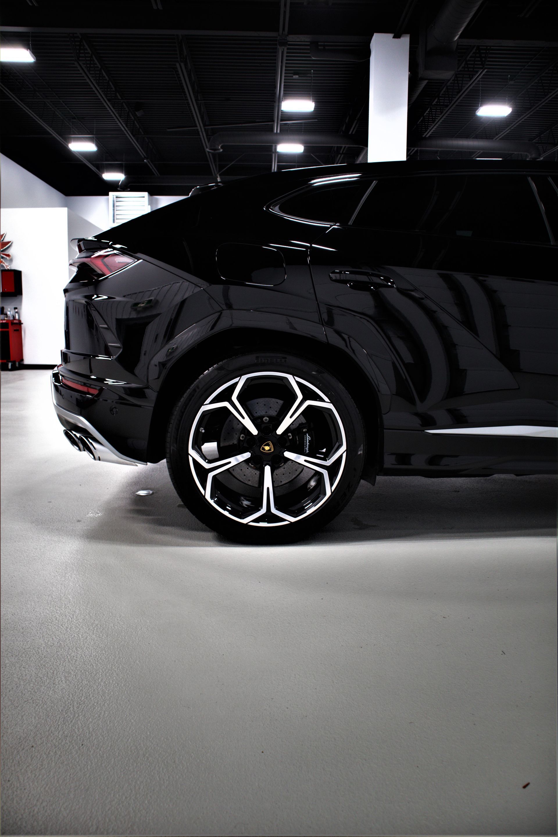 Black SUV in an indoor showroom, showing the rear side and chrome wheel.