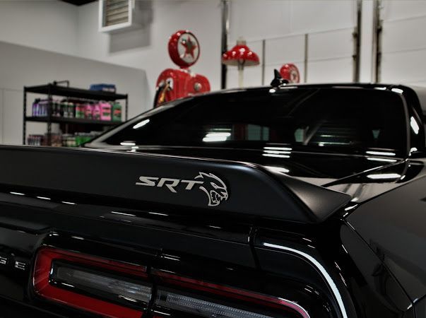 Black Dodge SRT car parked in a garage, showing the rear badge and taillights