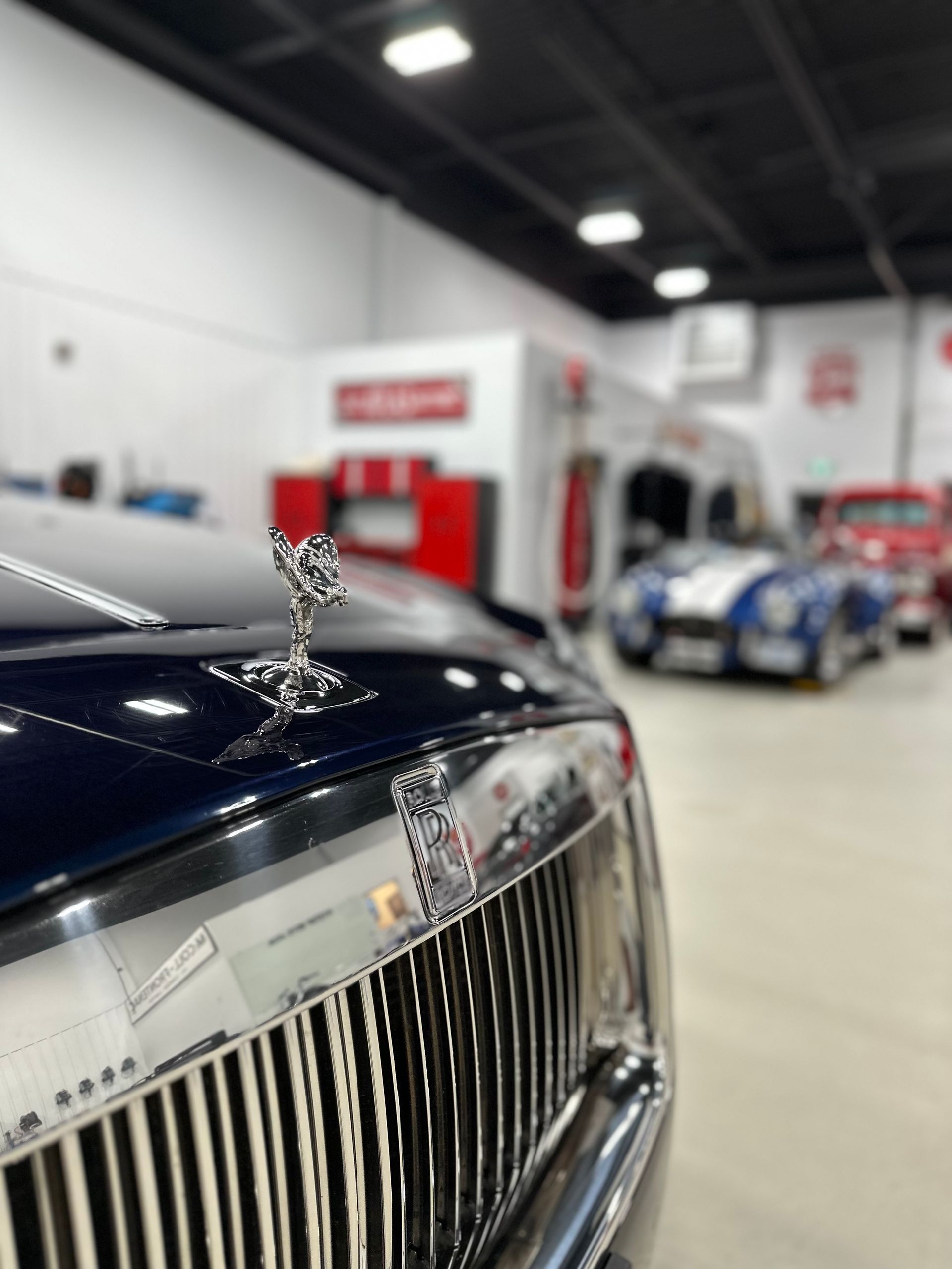 Silver hood ornament on a dark luxury car in an indoor showroom
