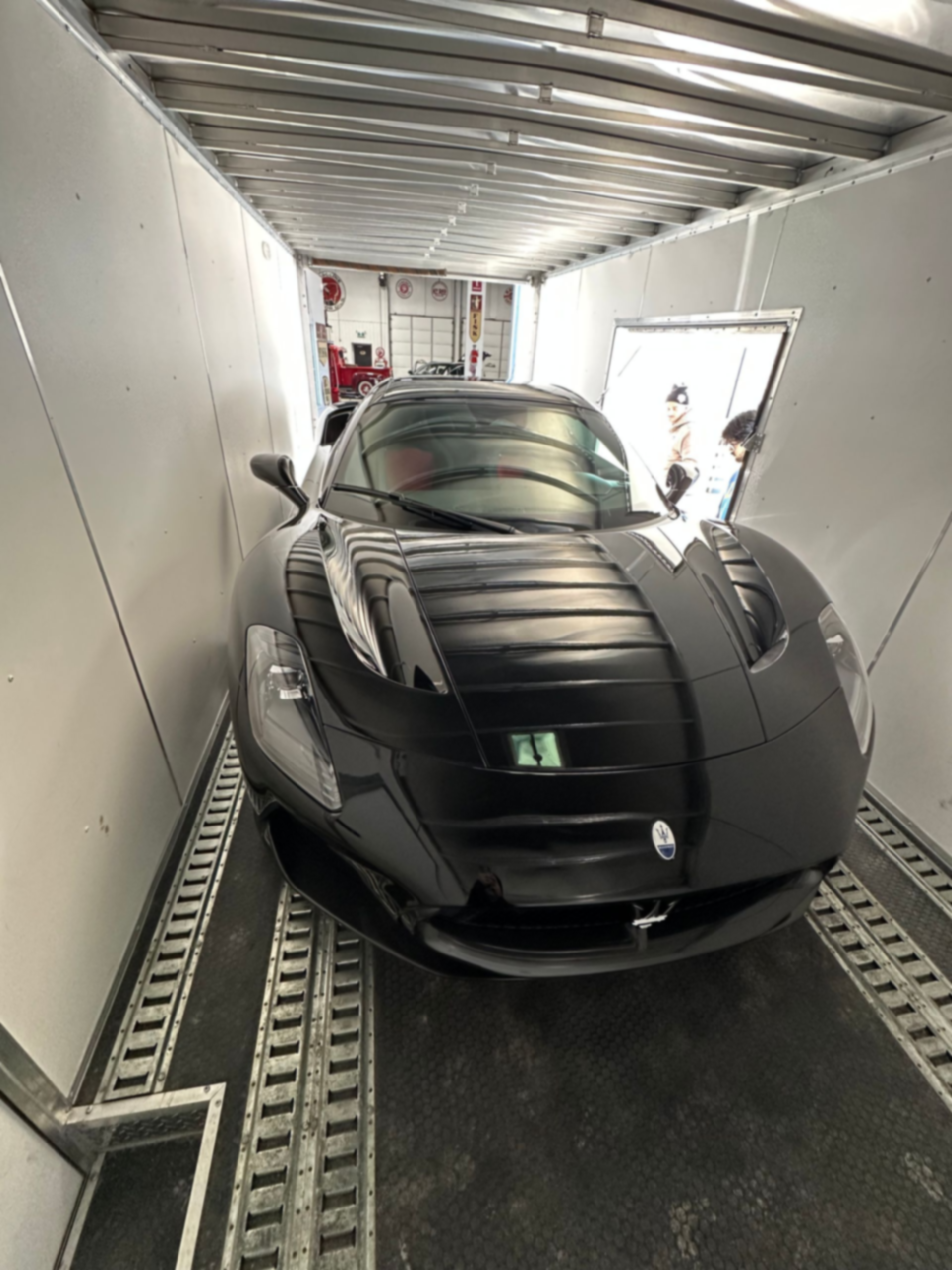 Black sports car inside a transport trailer, viewed from the rear.
