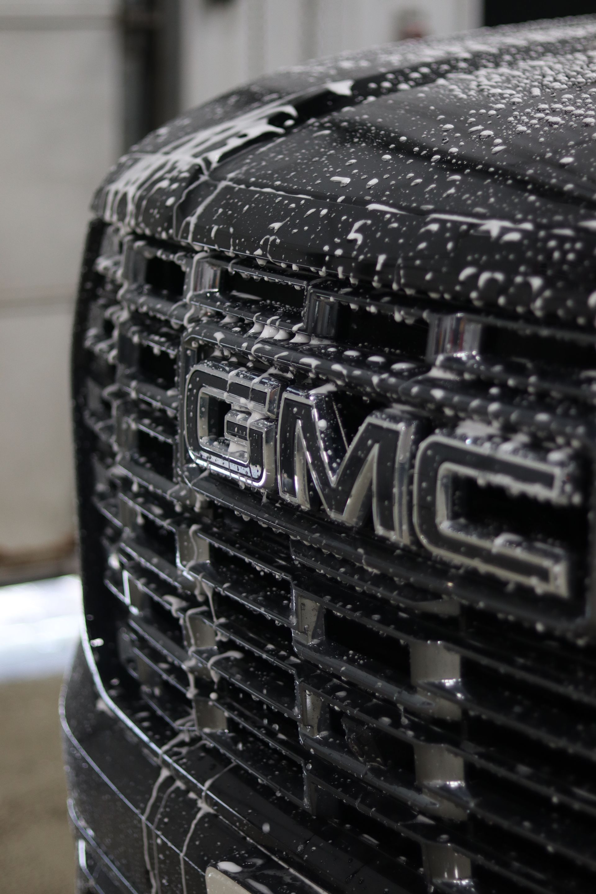 Close-up of a black GMC truck grille covered in water droplets.