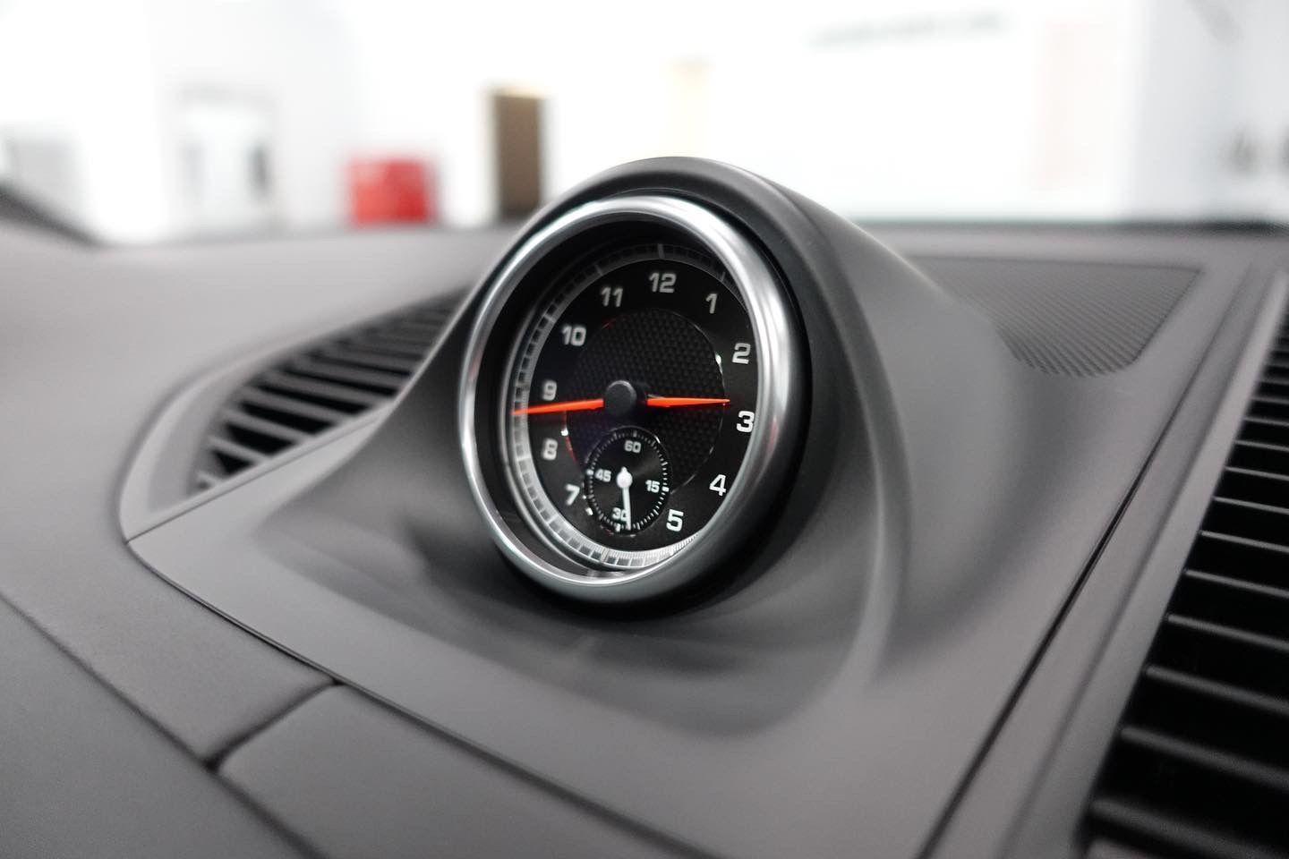 Round analog clock mounted on a car dashboard, set into a gray interior panel.