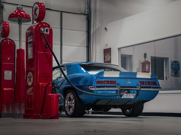 Blue classic muscle car beside vintage red gas pumps in a garage