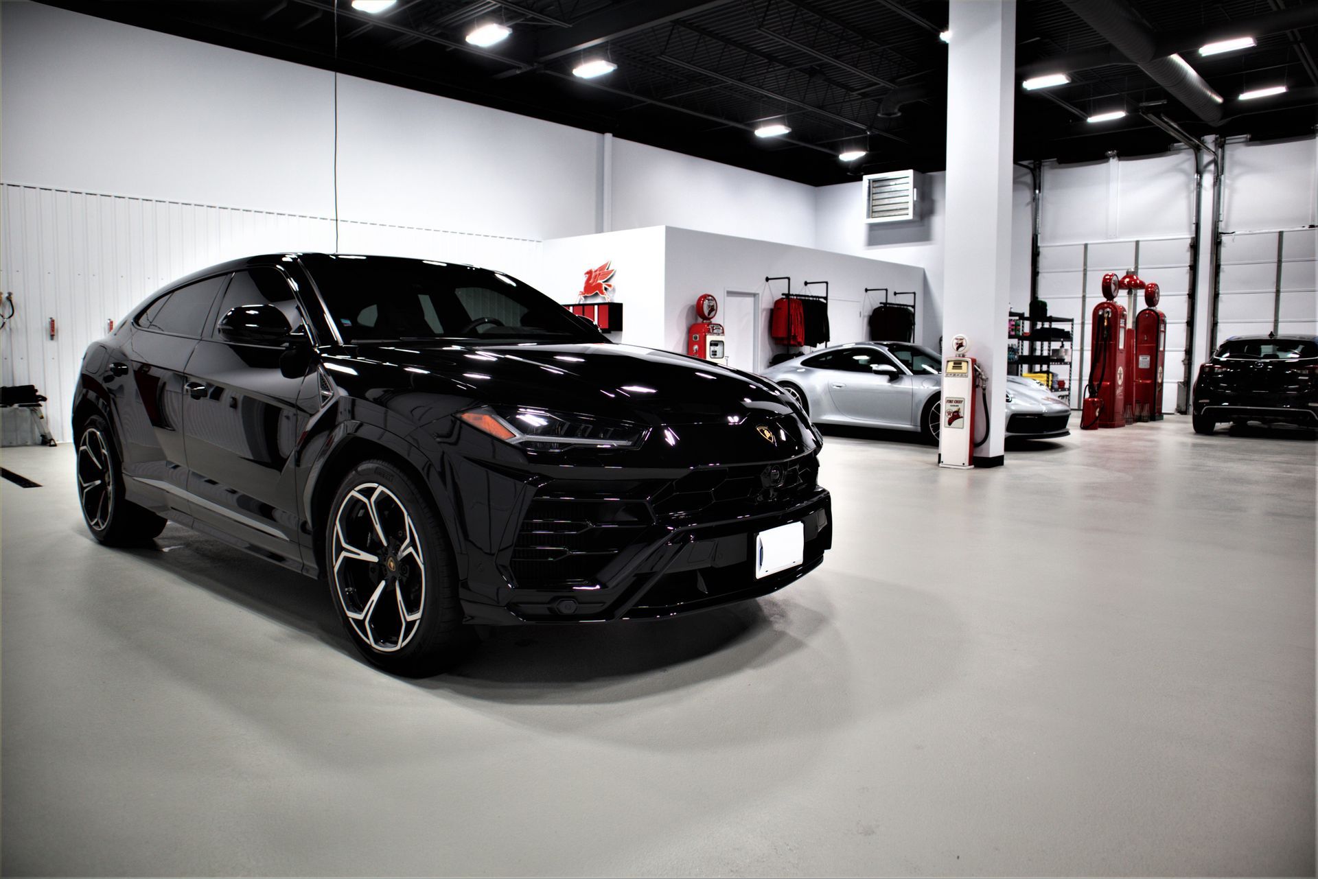 Black sports car in a bright auto shop garage with another car and equipment in the background