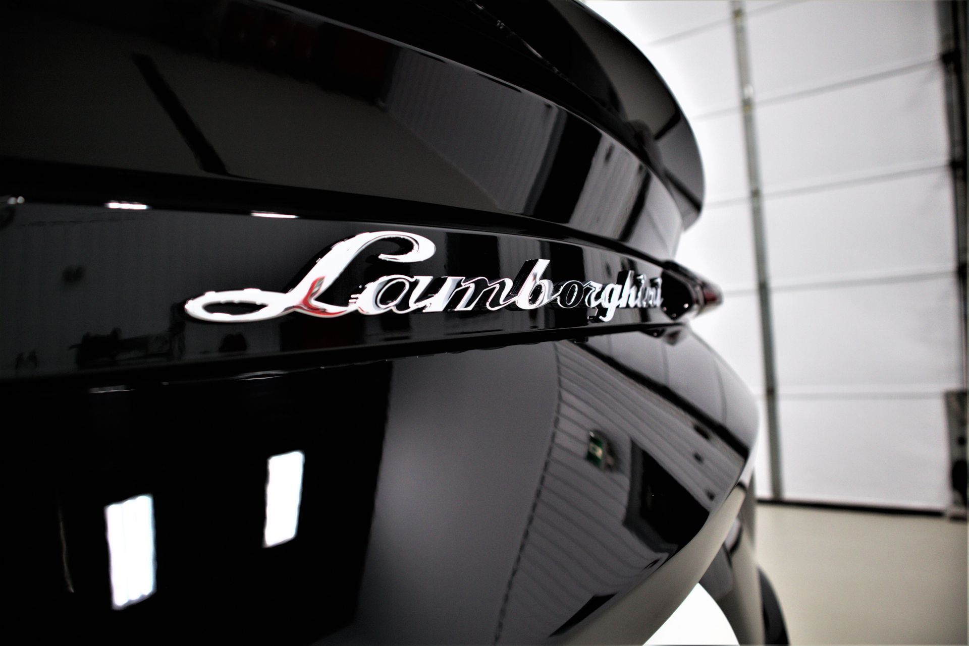 Close-up of a glossy black Lamborghini badge on a car in a garage