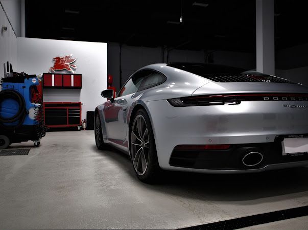 Silver sports car parked in a dim garage beside a blue forklift and red shelving