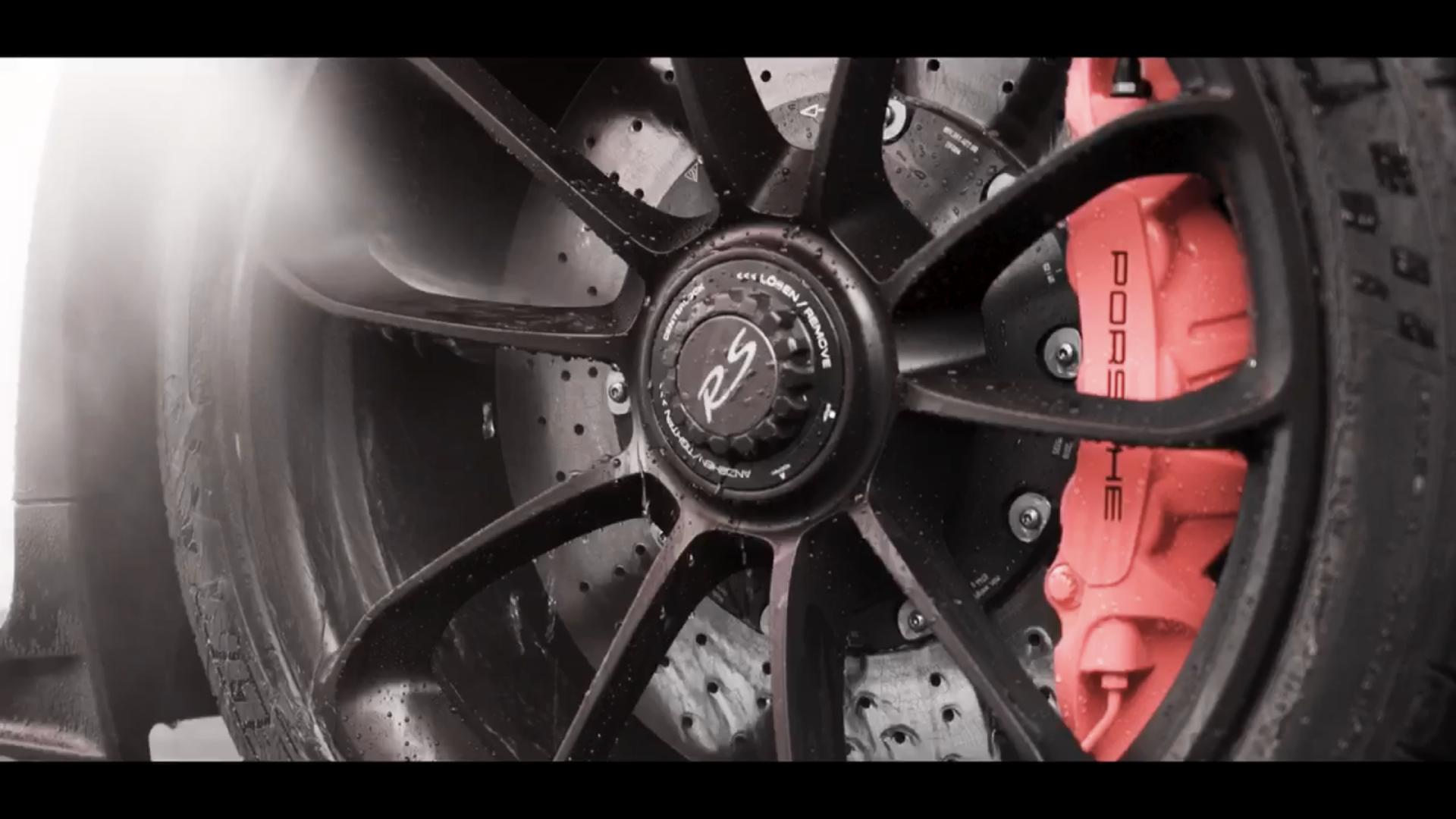Close-up of a black Porsche wheel with a red brake caliper and wet tire surface