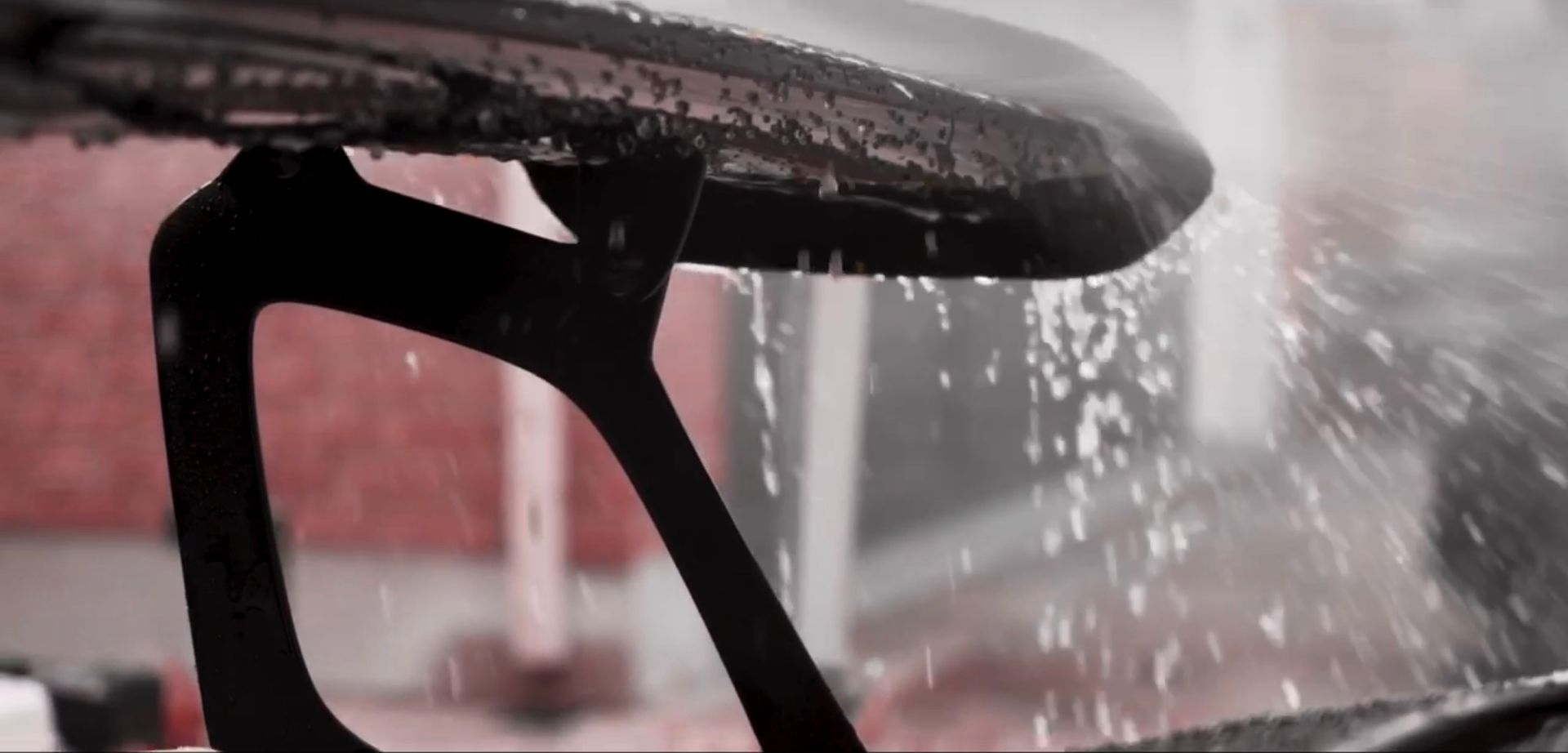 Black car side mirror with raindrops and water spray in the foreground