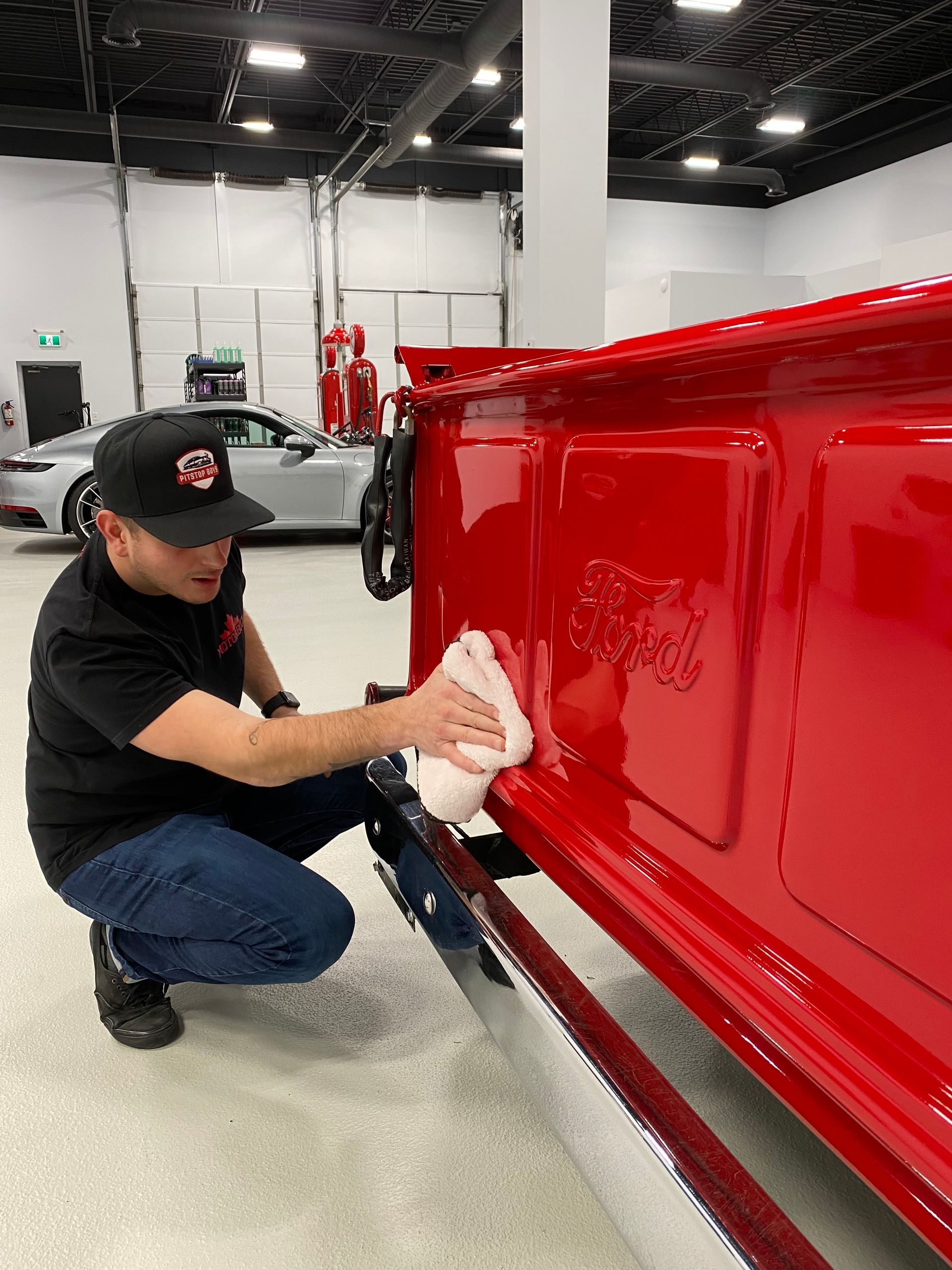 Person kneeling to polish a glossy red car panel in a garage