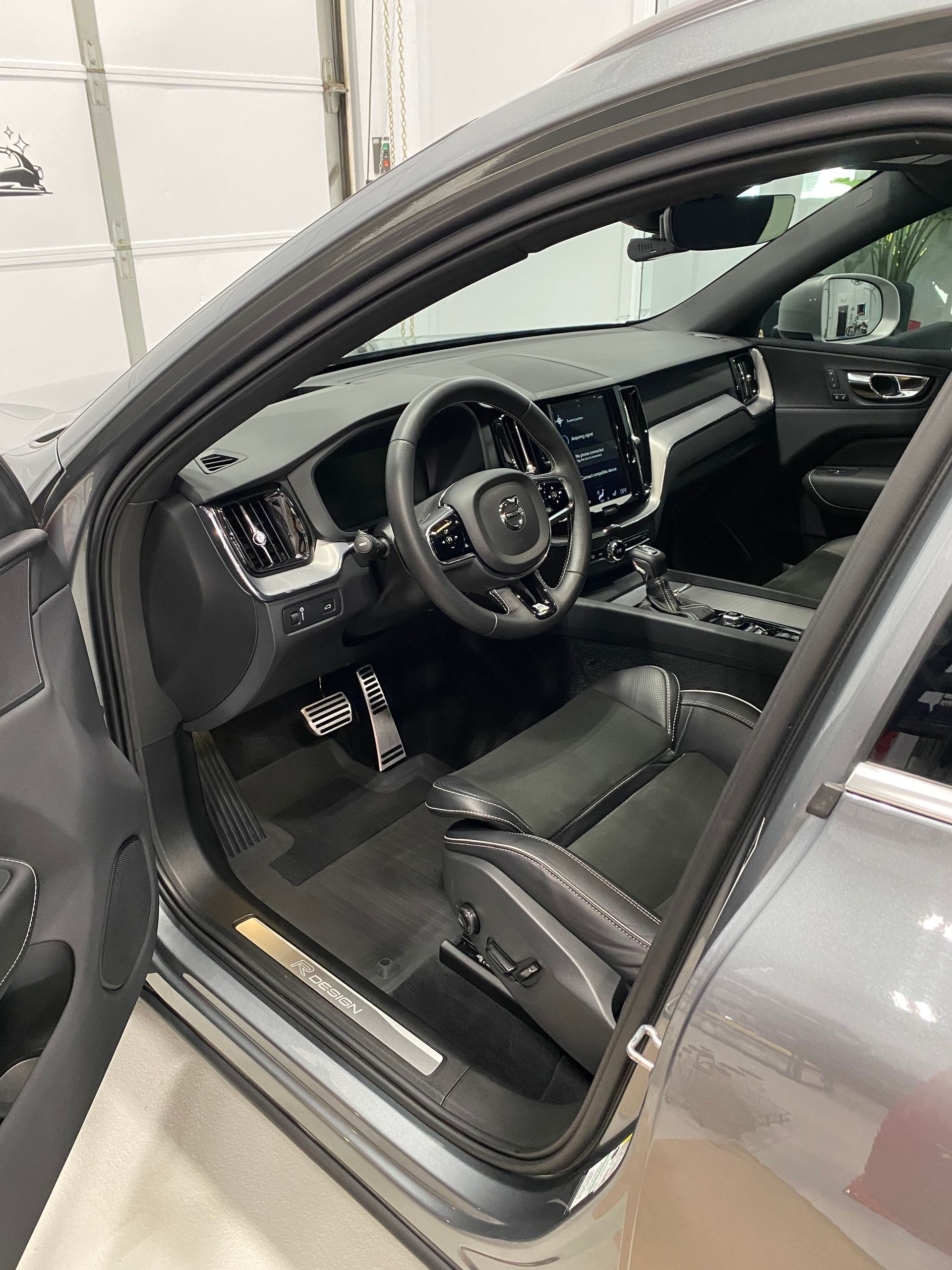 Gray car interior with open driver’s door, showing black leather seats and steering wheel inside a garage.