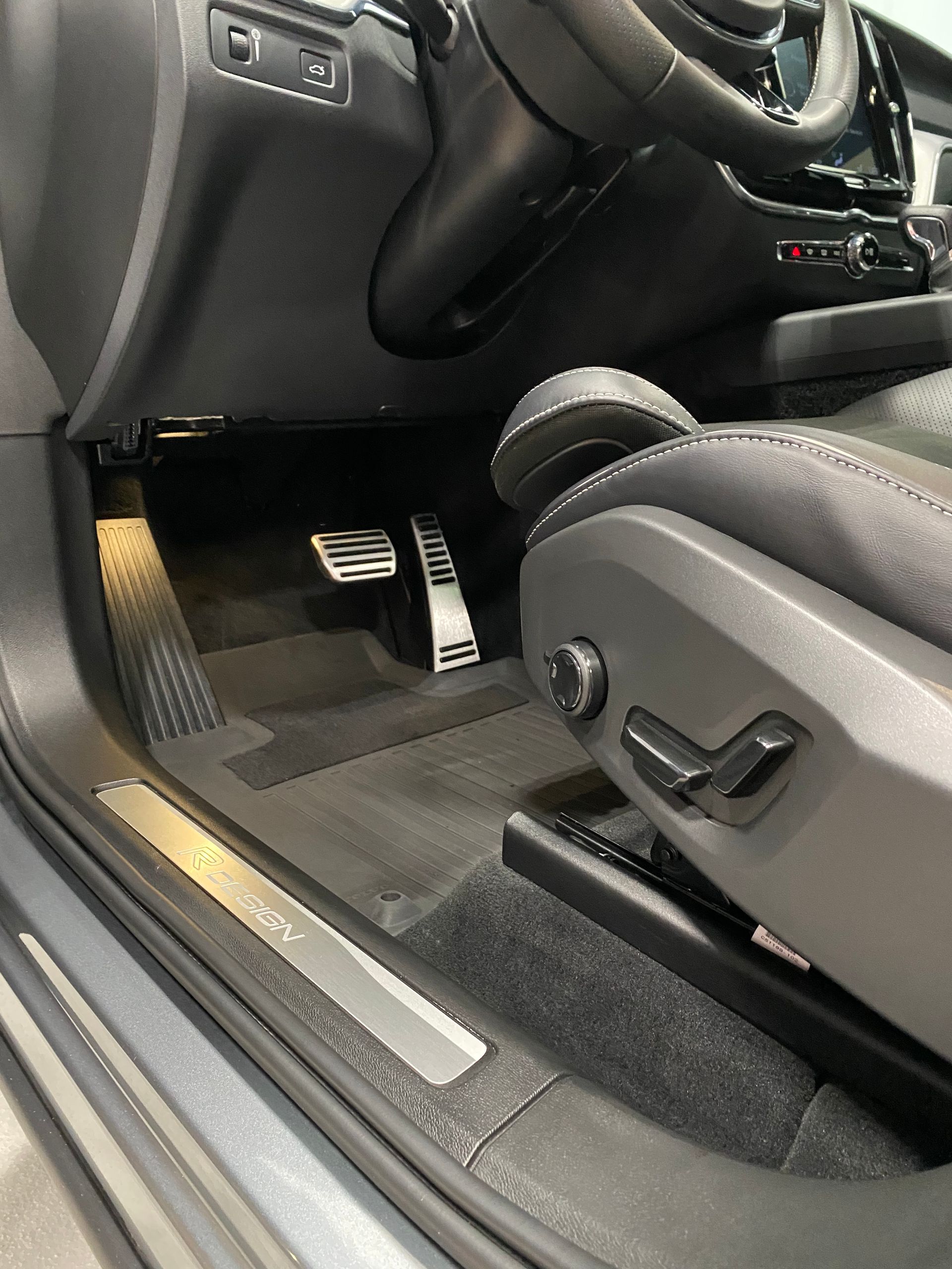 Car interior showing the driver’s footwell, black seats, and open door sill with illuminated trim