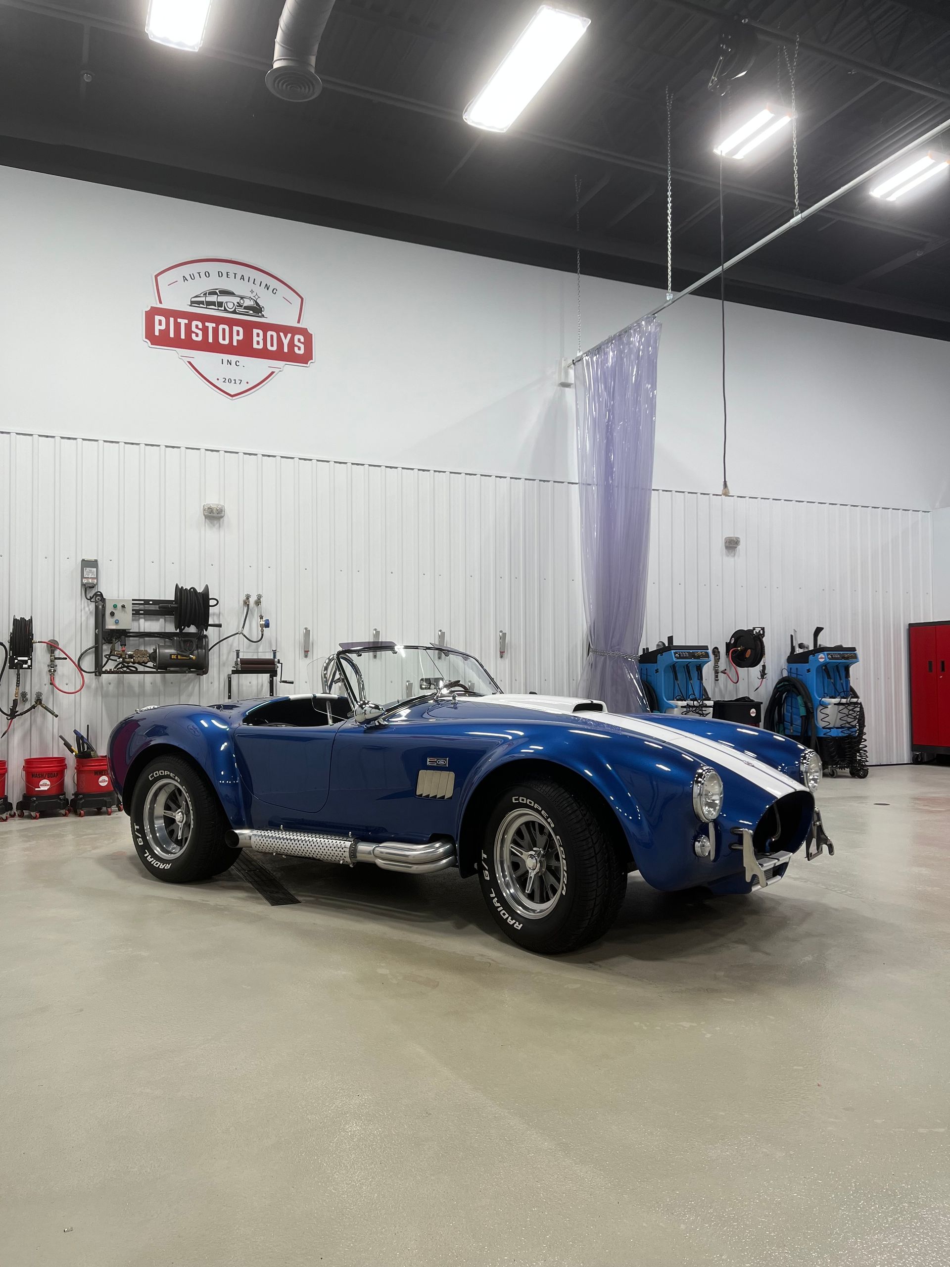 Blue classic sports car in a bright auto shop garage with tools and a lift in the background