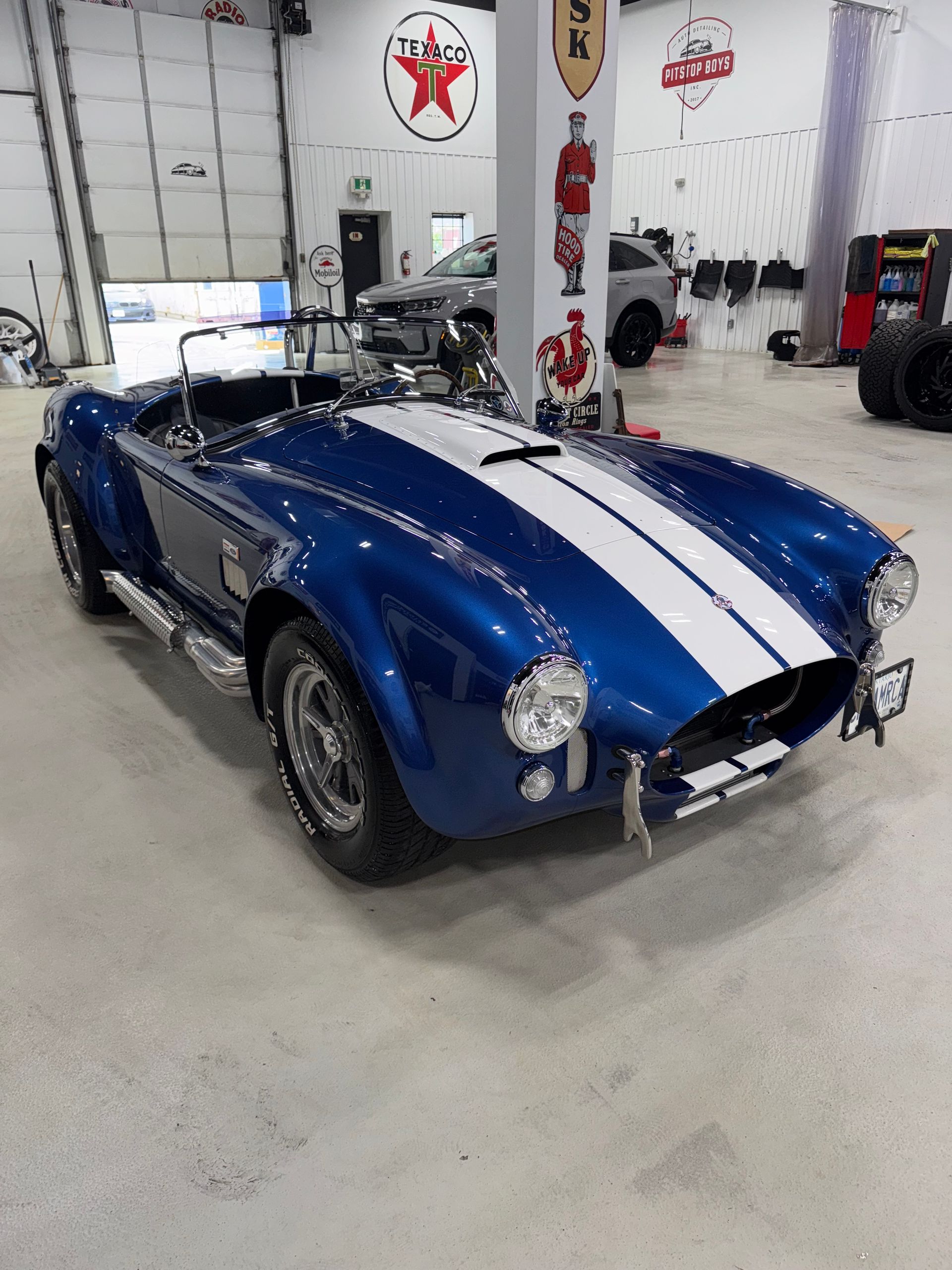 Blue classic Cobra sports car with white racing stripes in a garage showroom