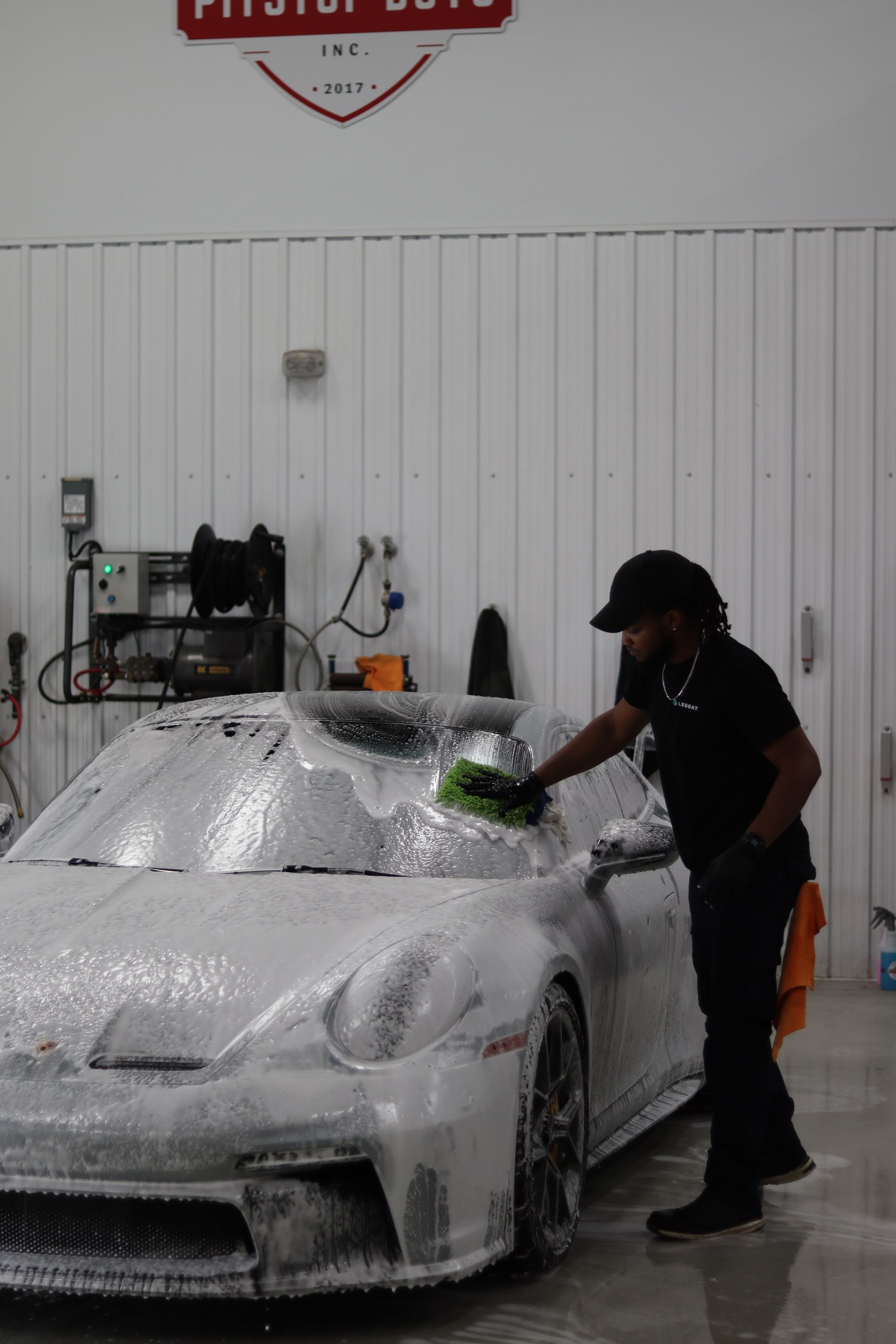 Person washing a foam-covered white car in a garage.
