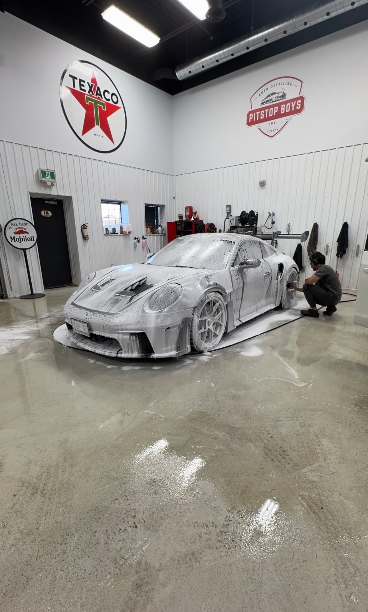 Foam-covered sports car being washed in a bright auto detailing garage