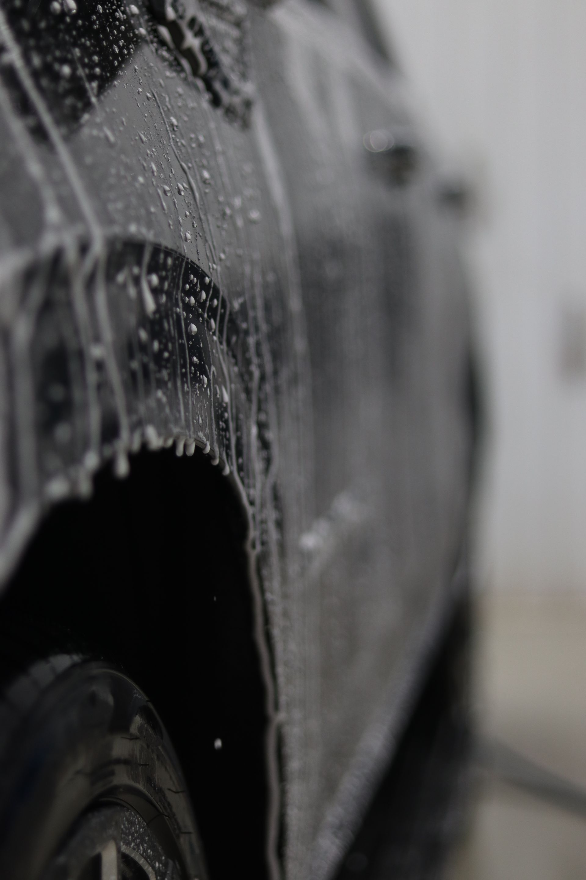 Close-up of a gray car covered in water droplets, with a blurred background