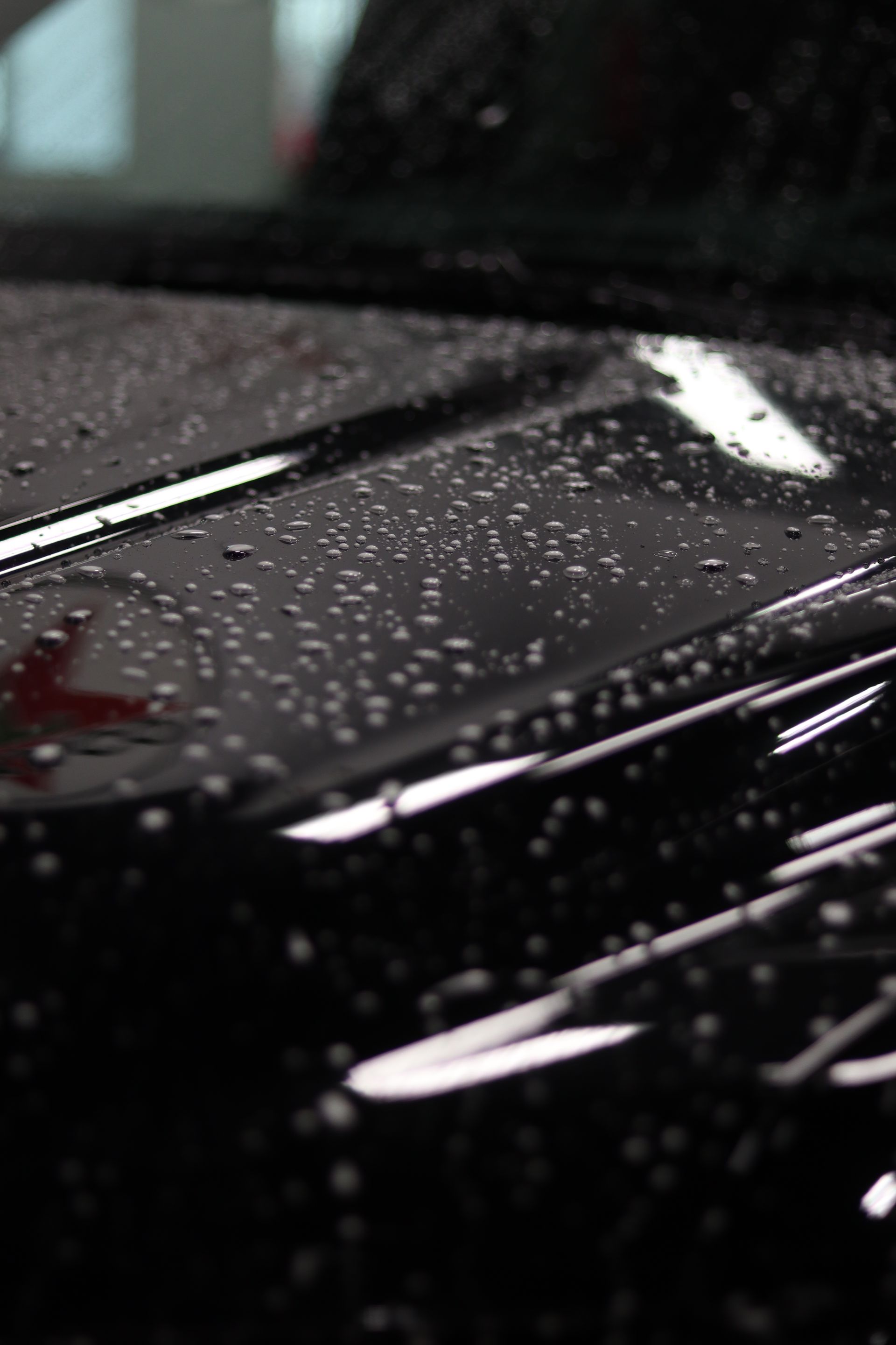 Rain droplets on a glossy black car hood with reflections of light.