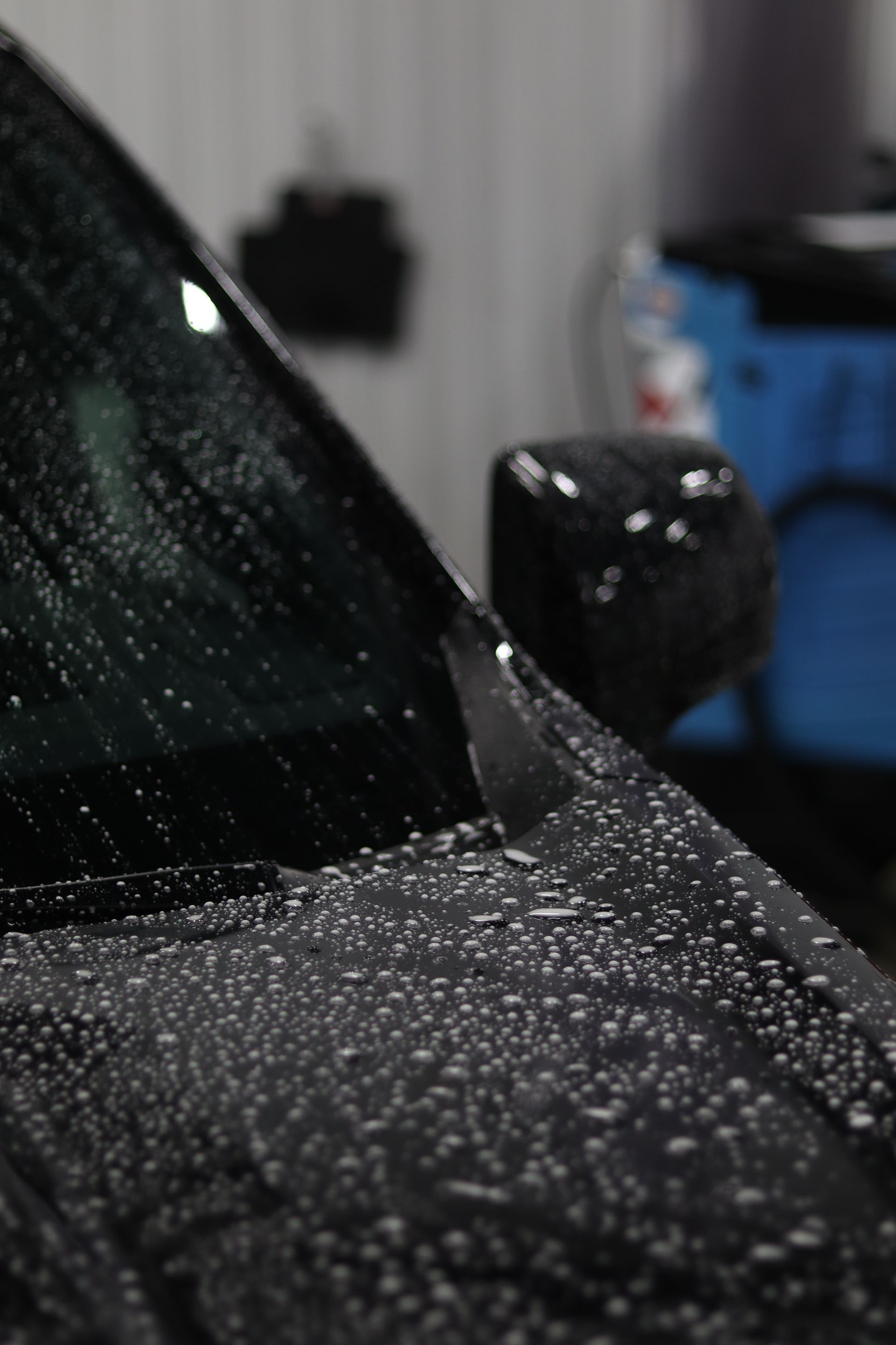 Rain-covered black car hood and side mirror in a garage