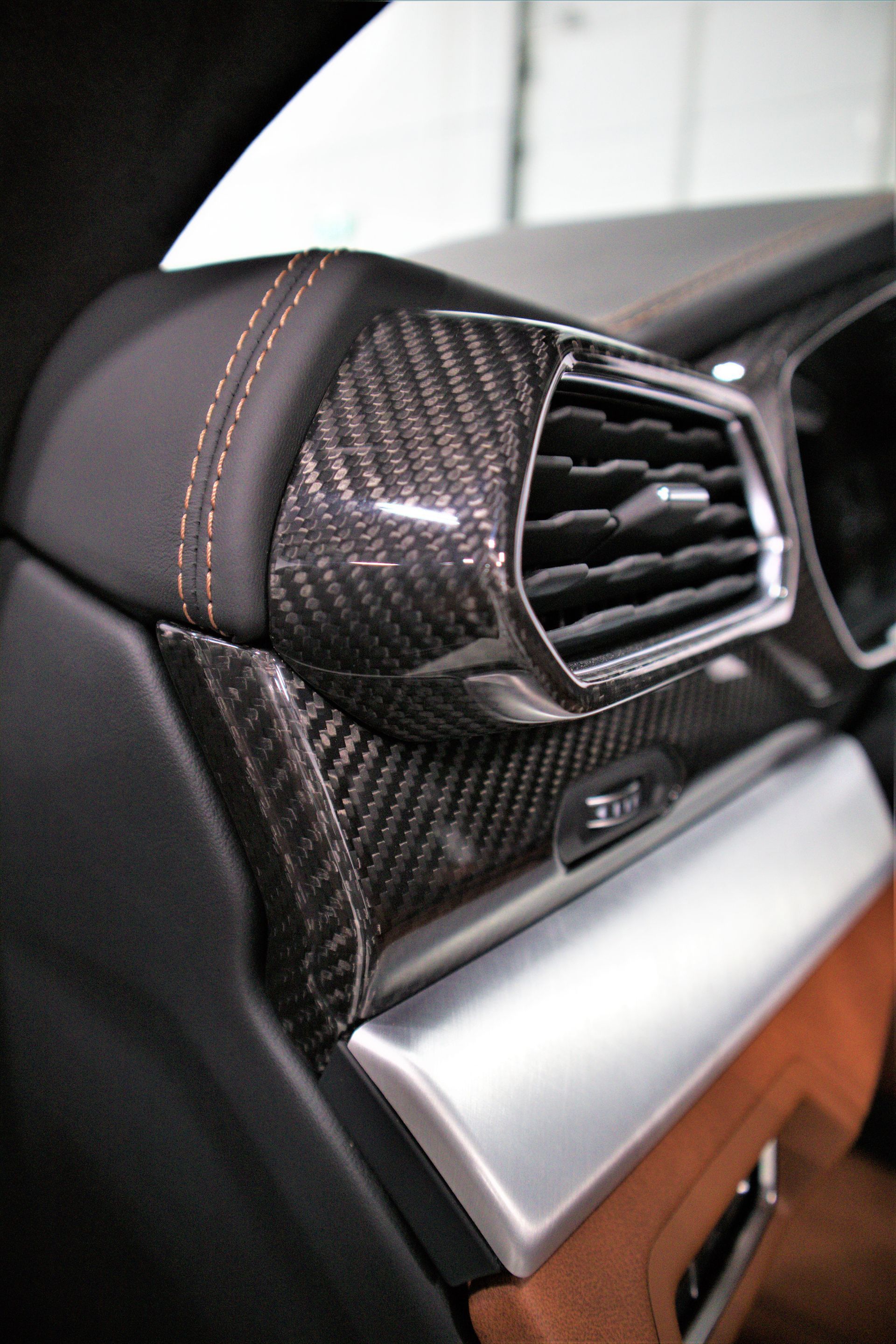 Close-up of a carbon-fiber car air vent and dashboard trim with black leather and silver accent.