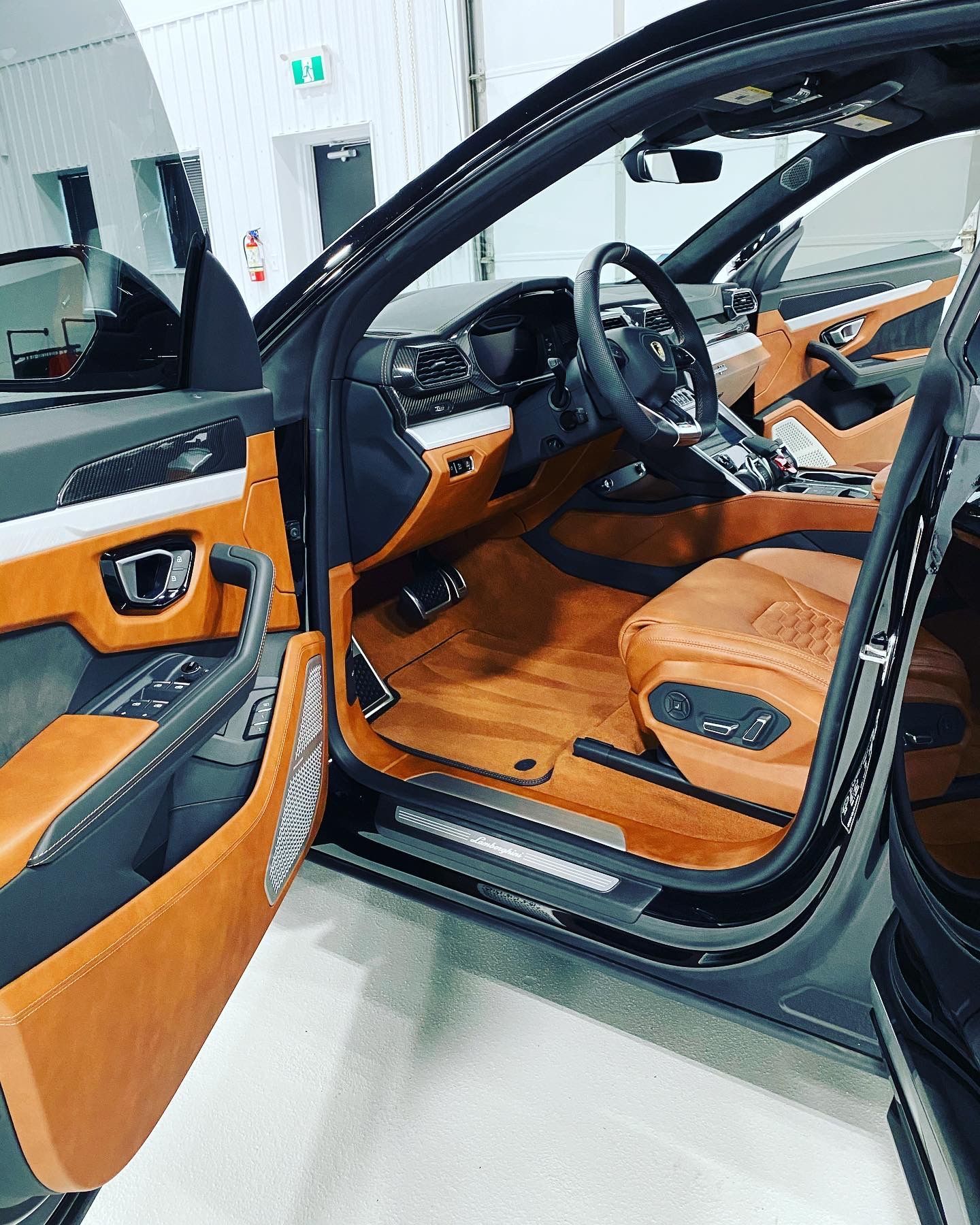 Luxury car interior with tan leather seats and open driver door, showing steering wheel and dashboard